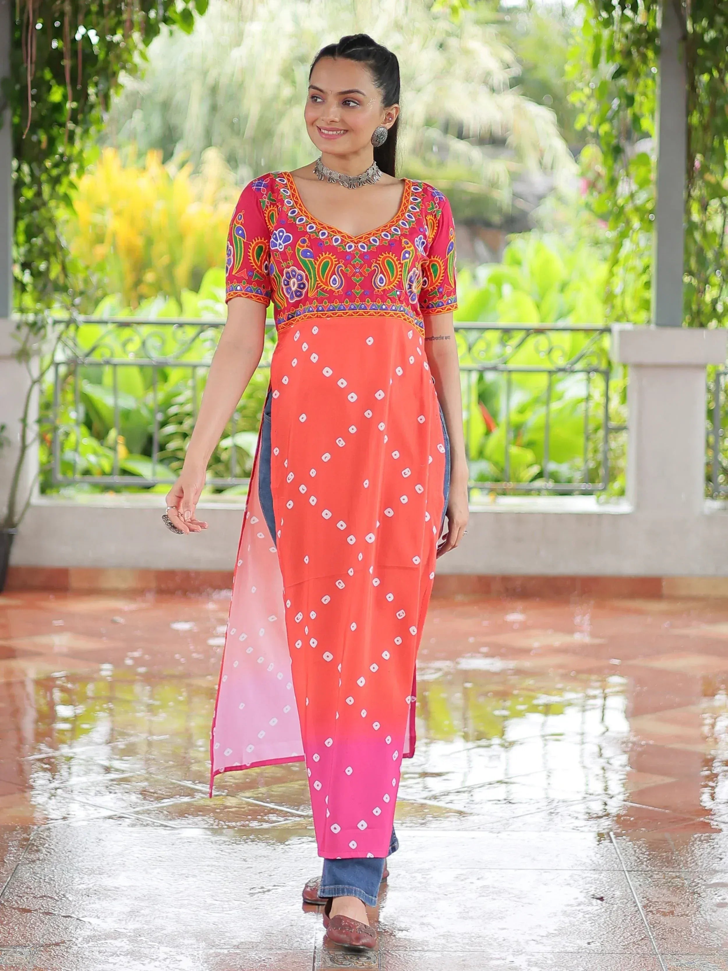 Woman in colorful embroidered kurta with bandhani print, styled with jeans and ethnic jewelry for festive occasions