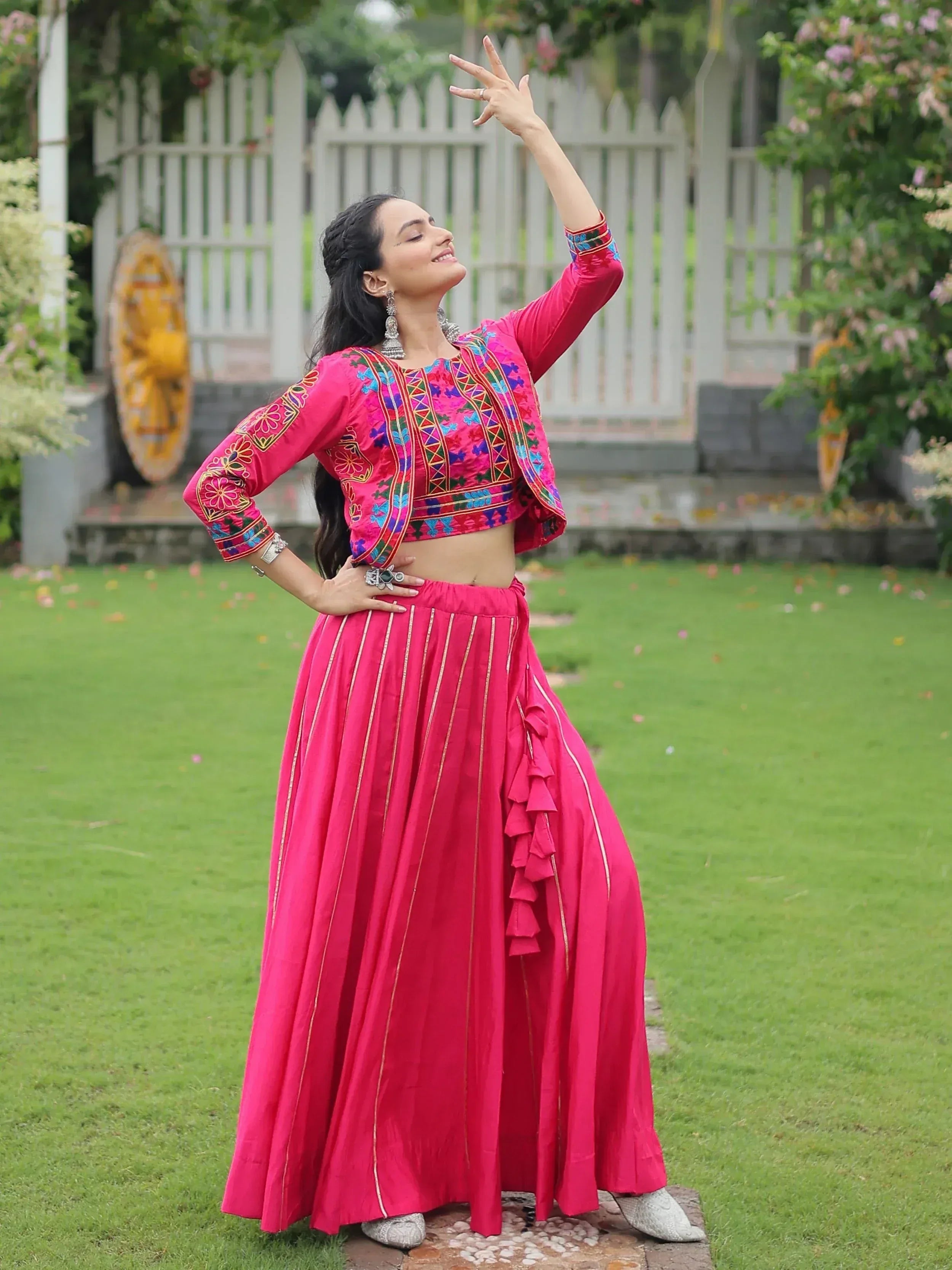 Woman in vibrant pink embroidered lehenga choli with ruffle skirt, posing outdoors on lawn