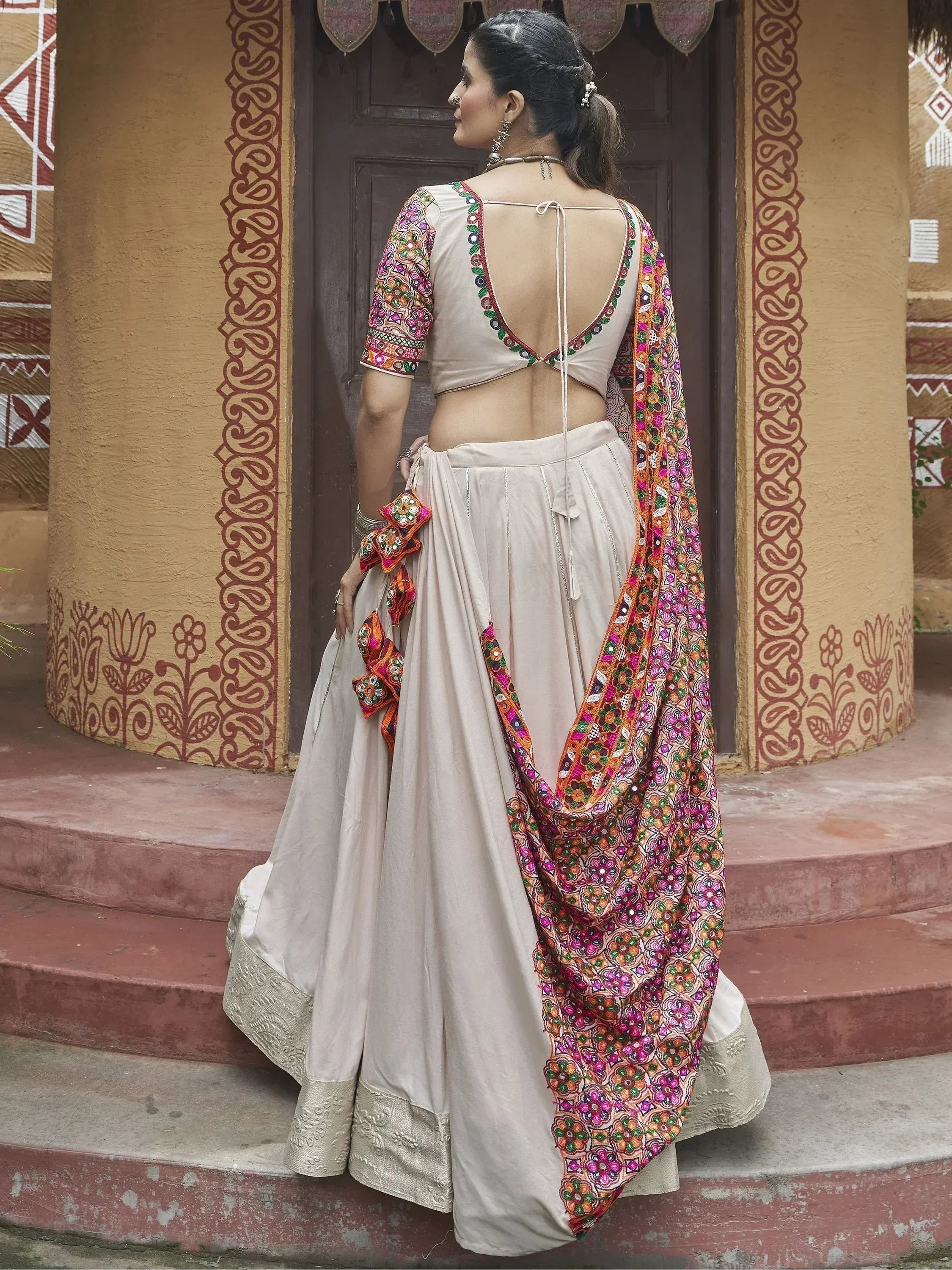 Beige embroidered lehenga choli with colorful mirror work dupatta, back view on steps