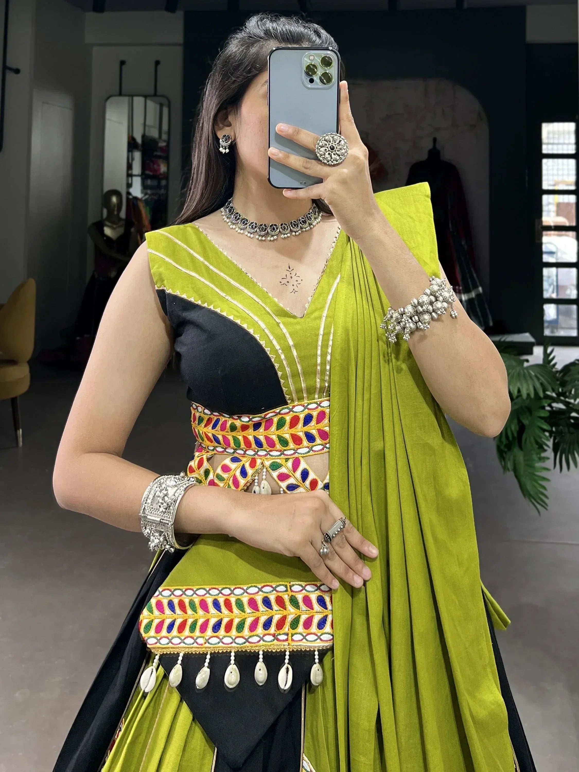 Woman in vibrant green and black ethnic lehenga choli with colorful mirror work and silver jewelry