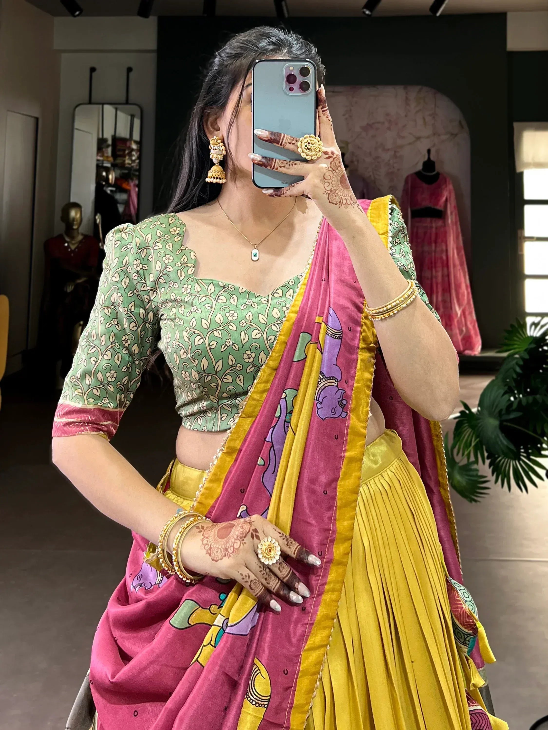Woman in vibrant Indian lehenga choli with floral blouse, pink and yellow dupatta, and traditional jewelry