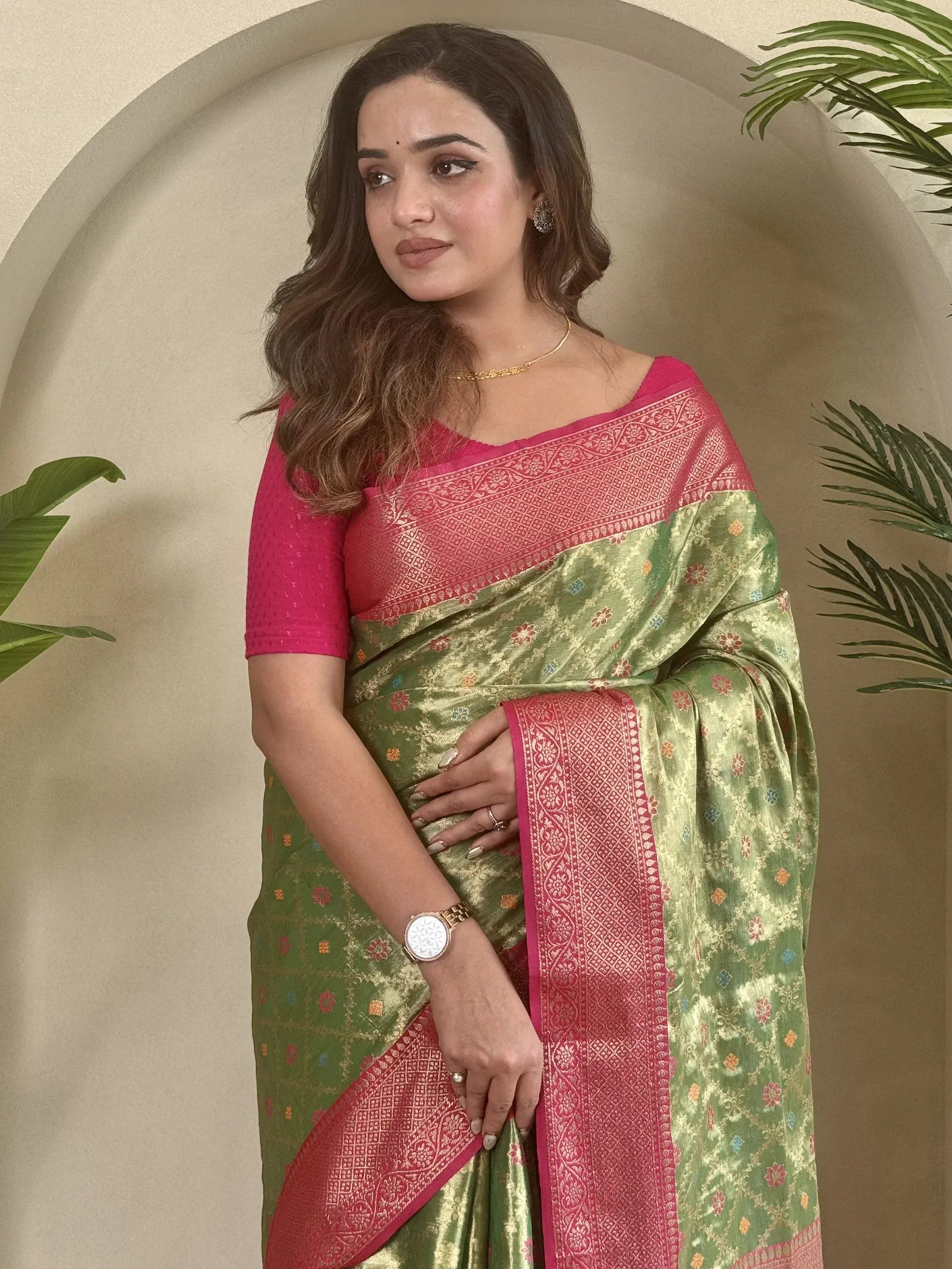 Woman in green and pink designer saree with floral motifs and gold border, styled with matching blouse for ethnic wear