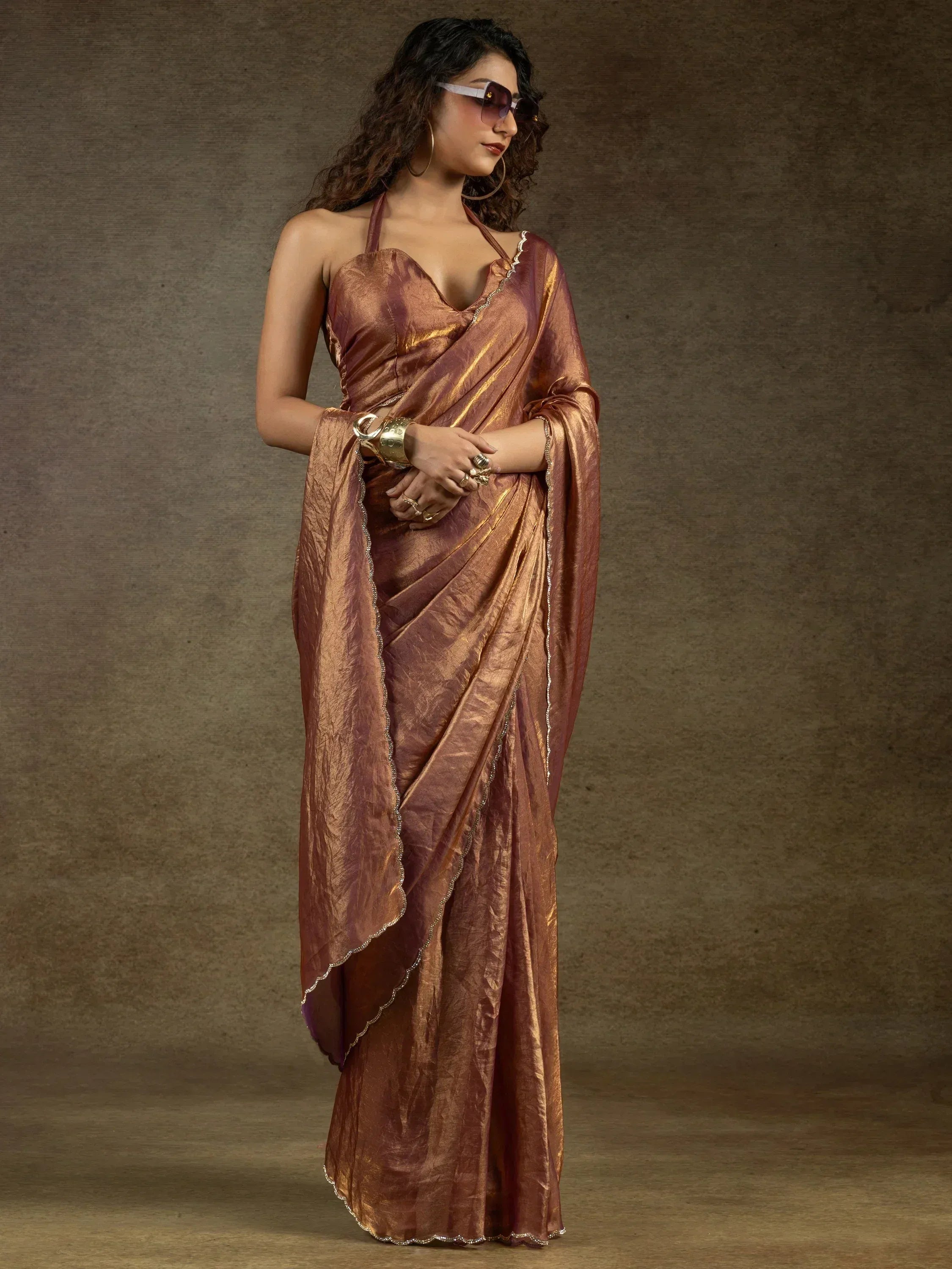 Woman in elegant copper saree with gold trim, stylish halter neck blouse, and statement jewelry