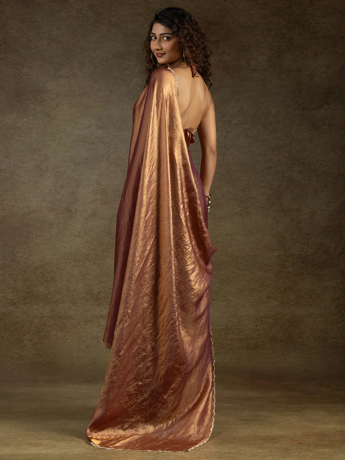 Elegant copper-toned ethnic gown with backless design and shimmering drape, perfect for Indian festive occasions.