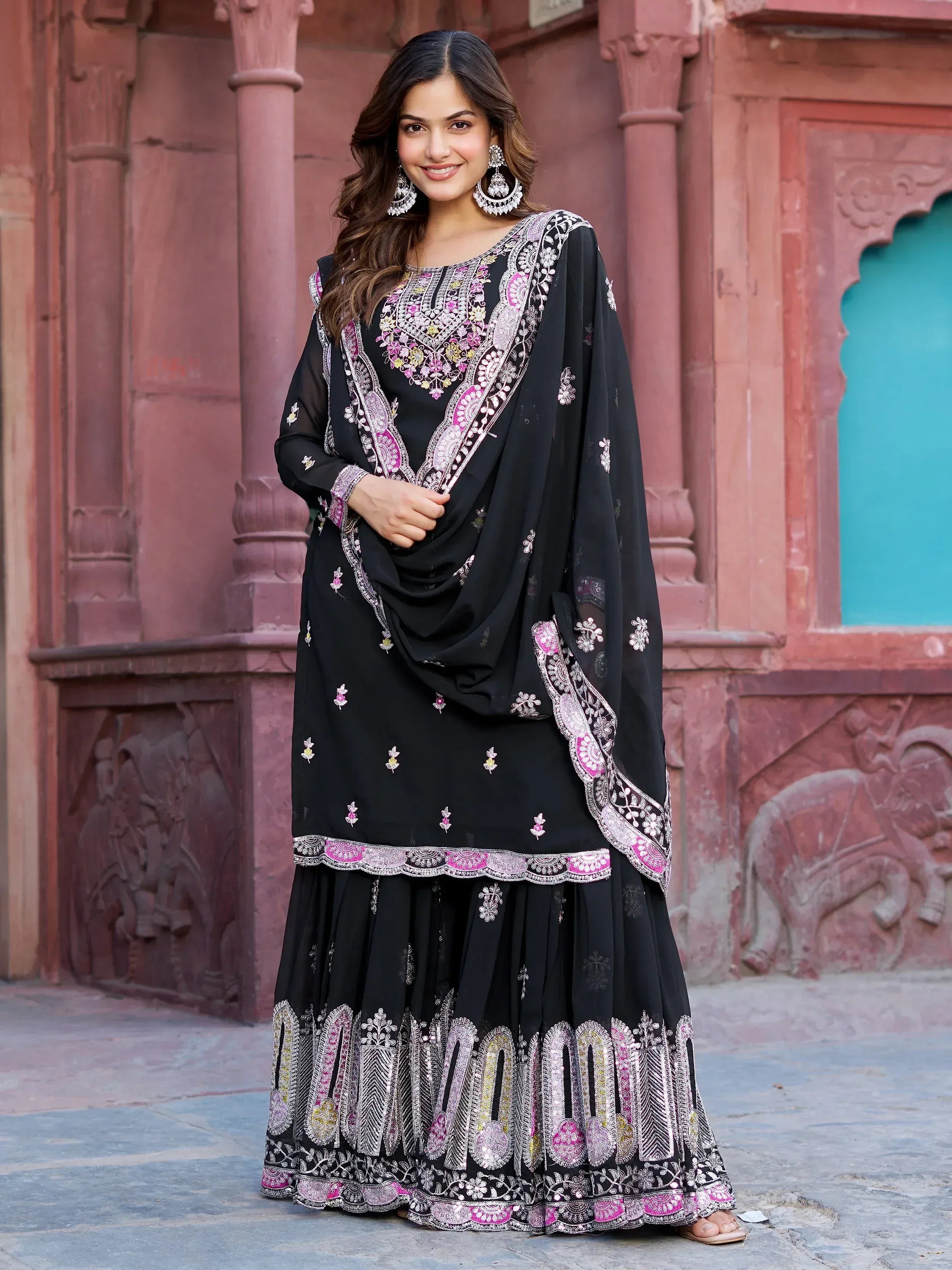 Black embroidered lehenga choli with pink and gold detailing, styled with traditional earrings