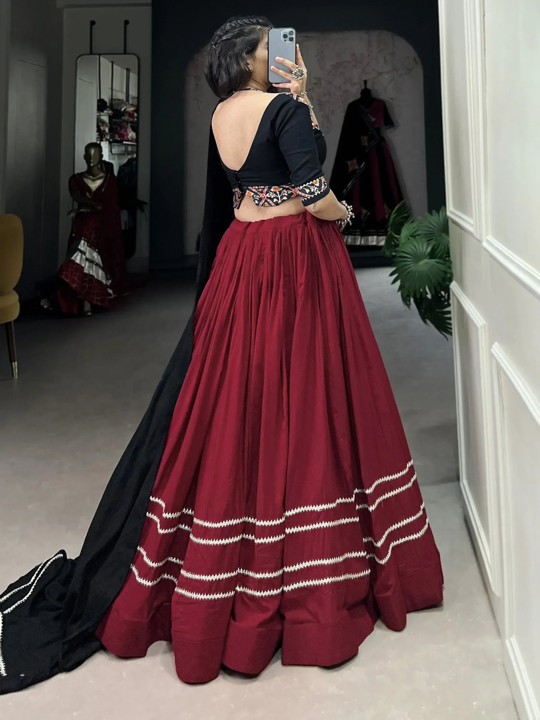 Woman in maroon and black lehenga choli with embroidered blouse, taking mirror selfie in boutique