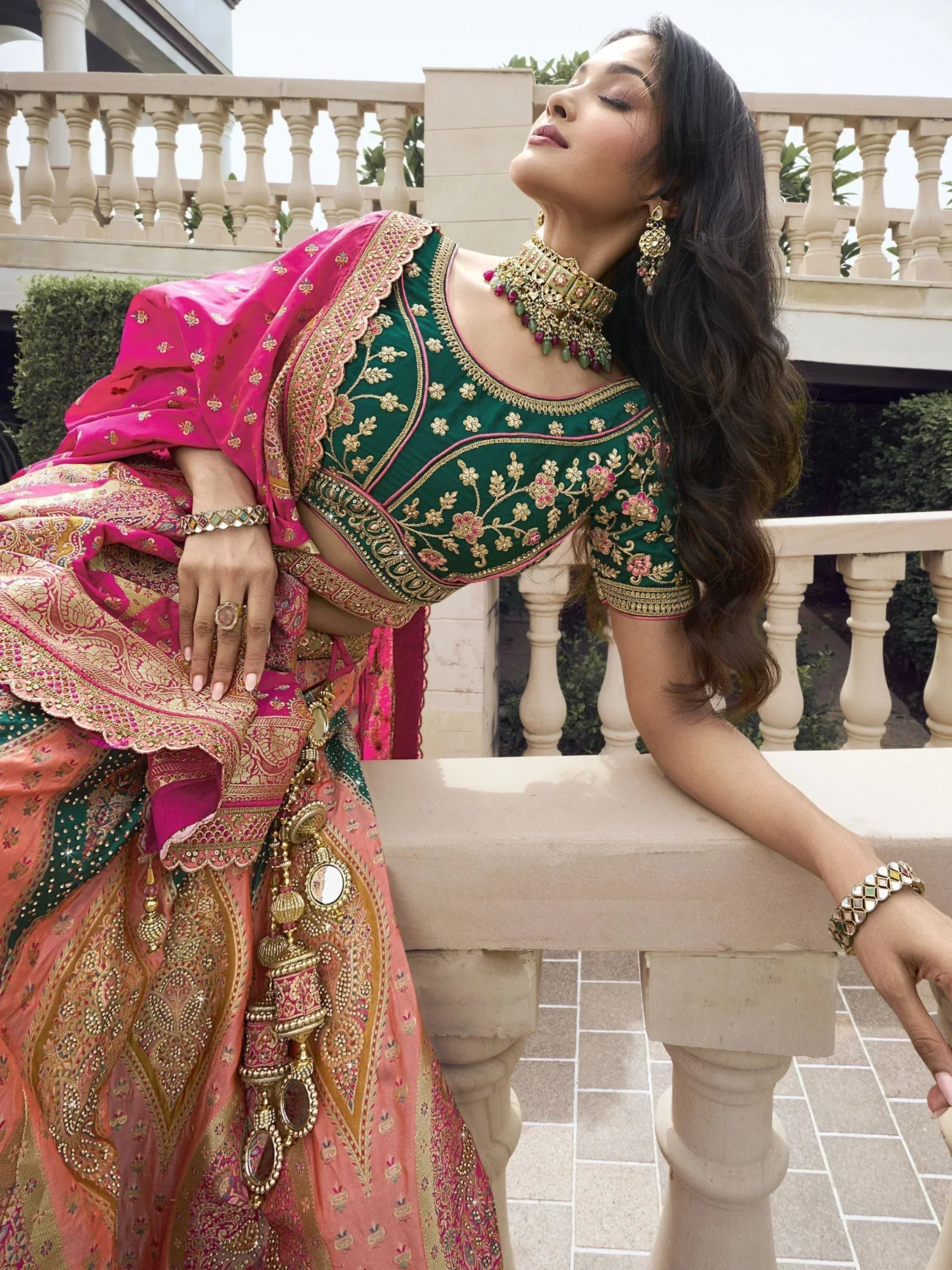 Woman in designer green and pink lehenga choli with gold embroidery, perfect for Indian ethnic wear occasions.