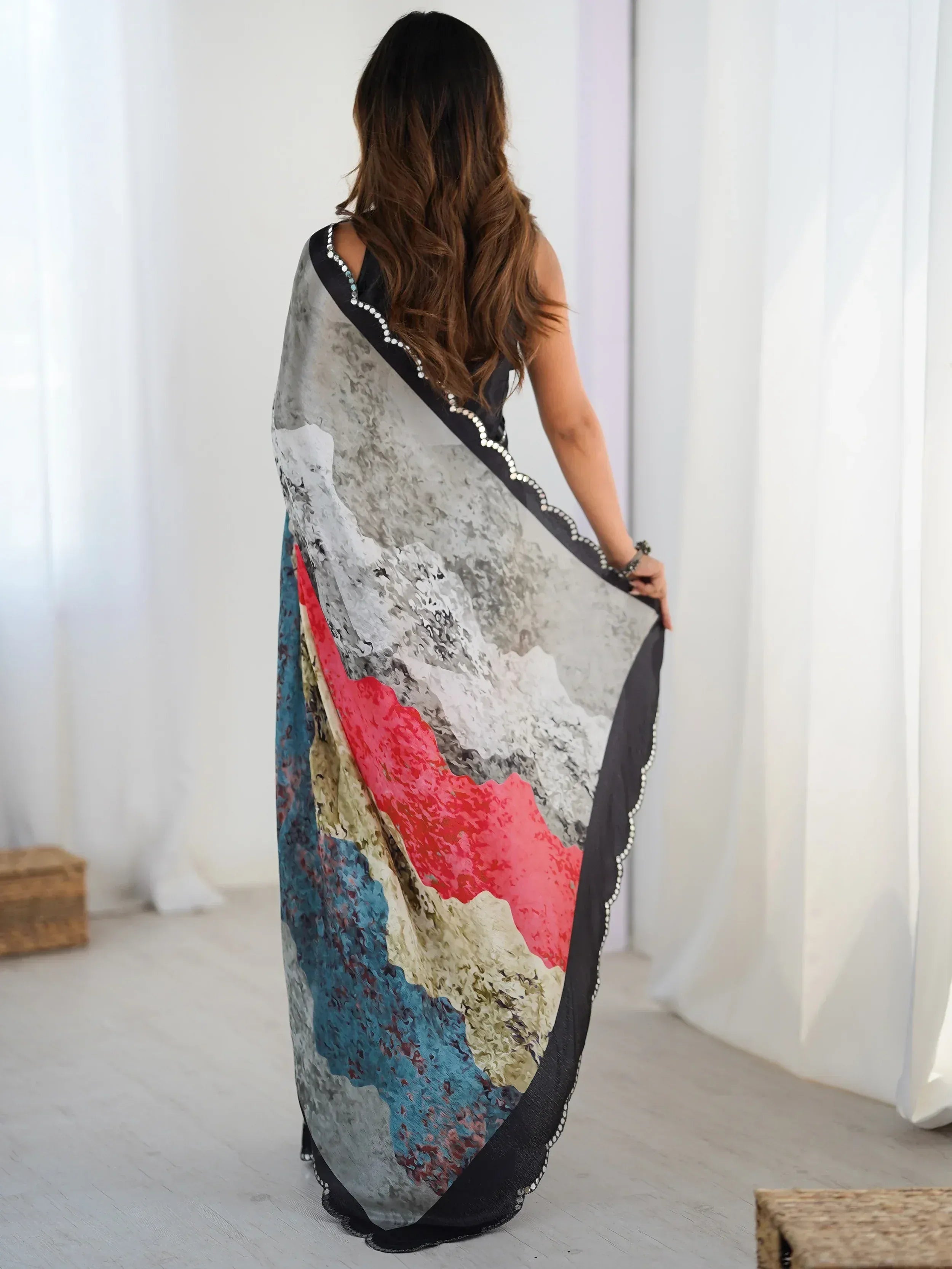 Woman wearing colorful abstract print saree with black border and embellishments, back view