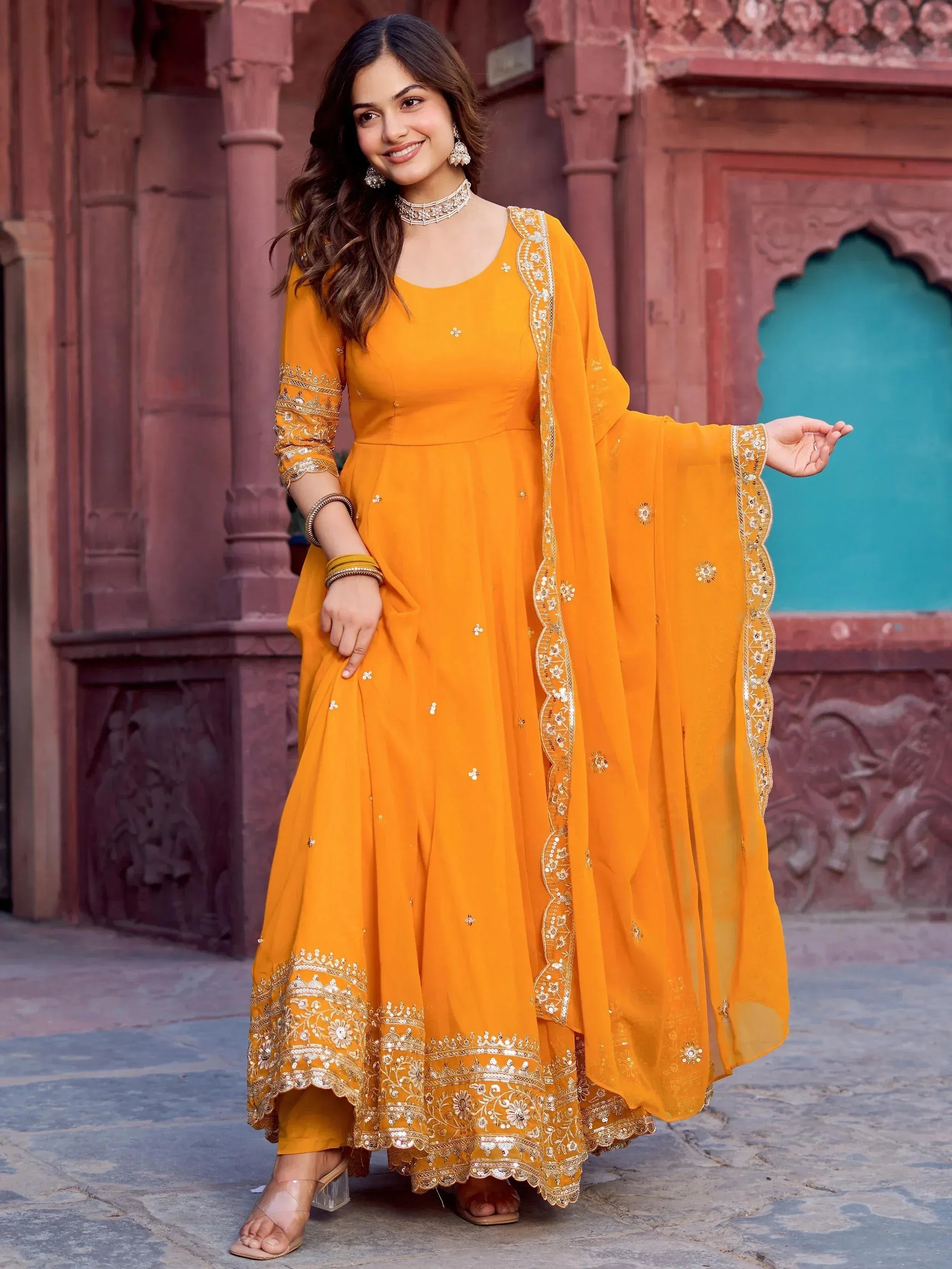 Vibrant orange ethnic gown with gold embroidery, perfect for Indian celebrations and festive occasions.