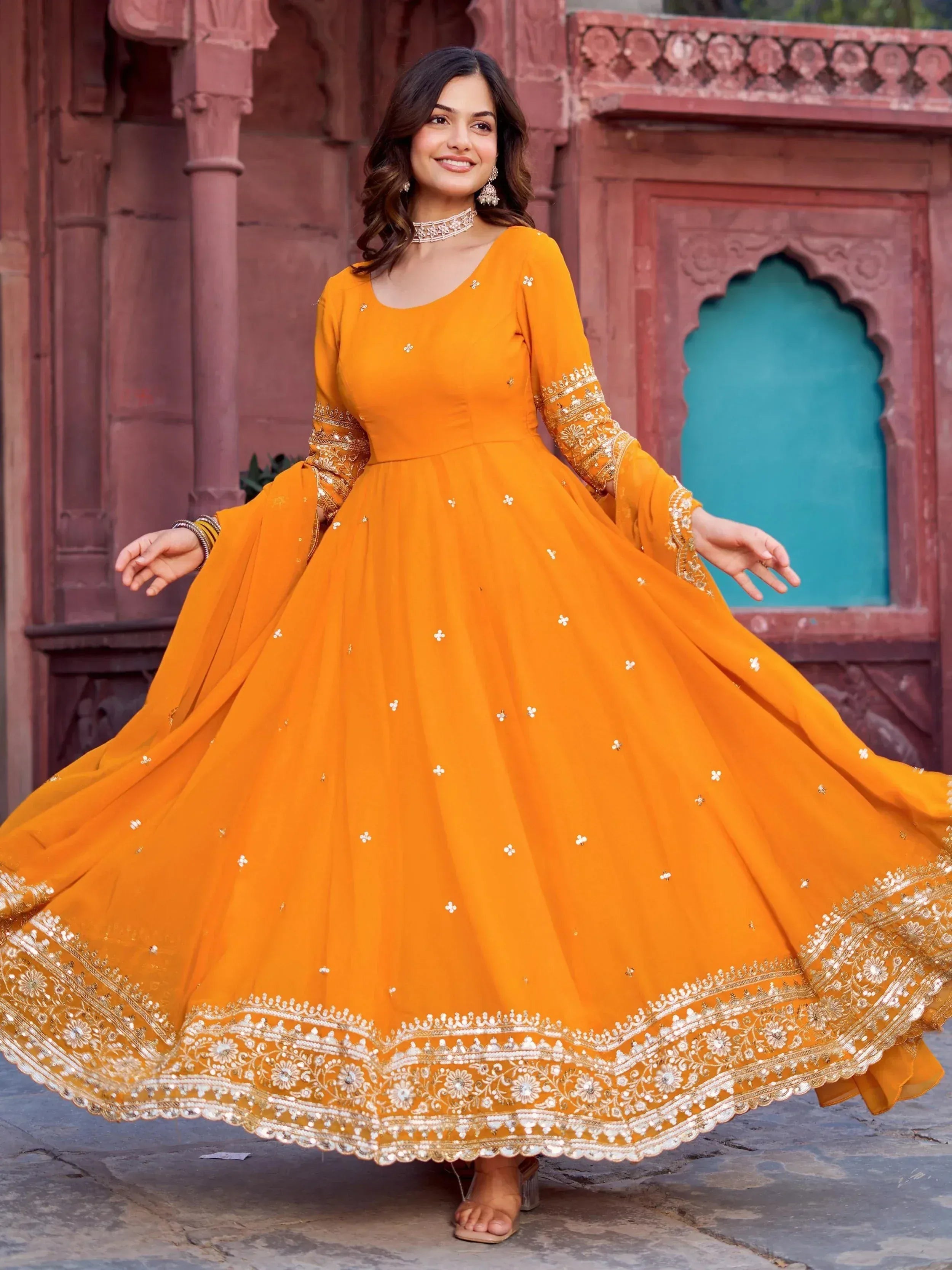 Vibrant orange ethnic gown with intricate gold embroidery, perfect for festive occasions and celebrations.