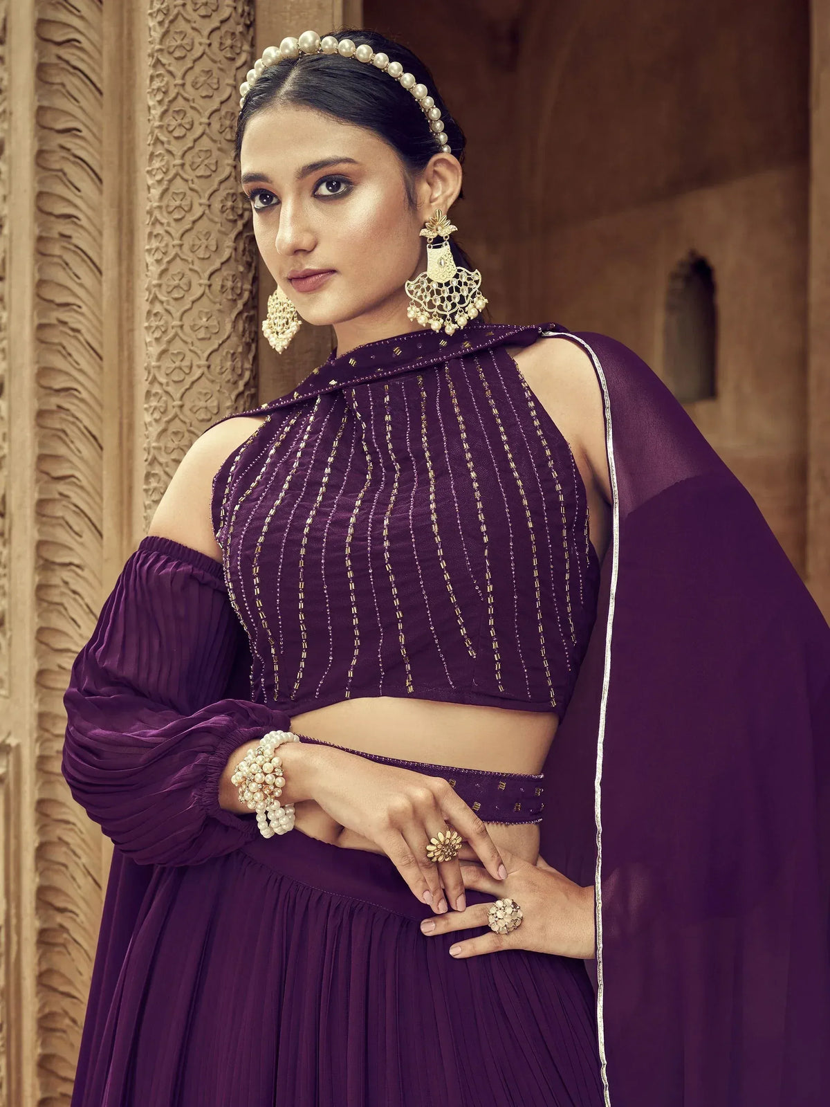 Purple designer lehenga choli with gold embroidery, pearl jewelry, and off-shoulder blouse for Indian ethnic wear