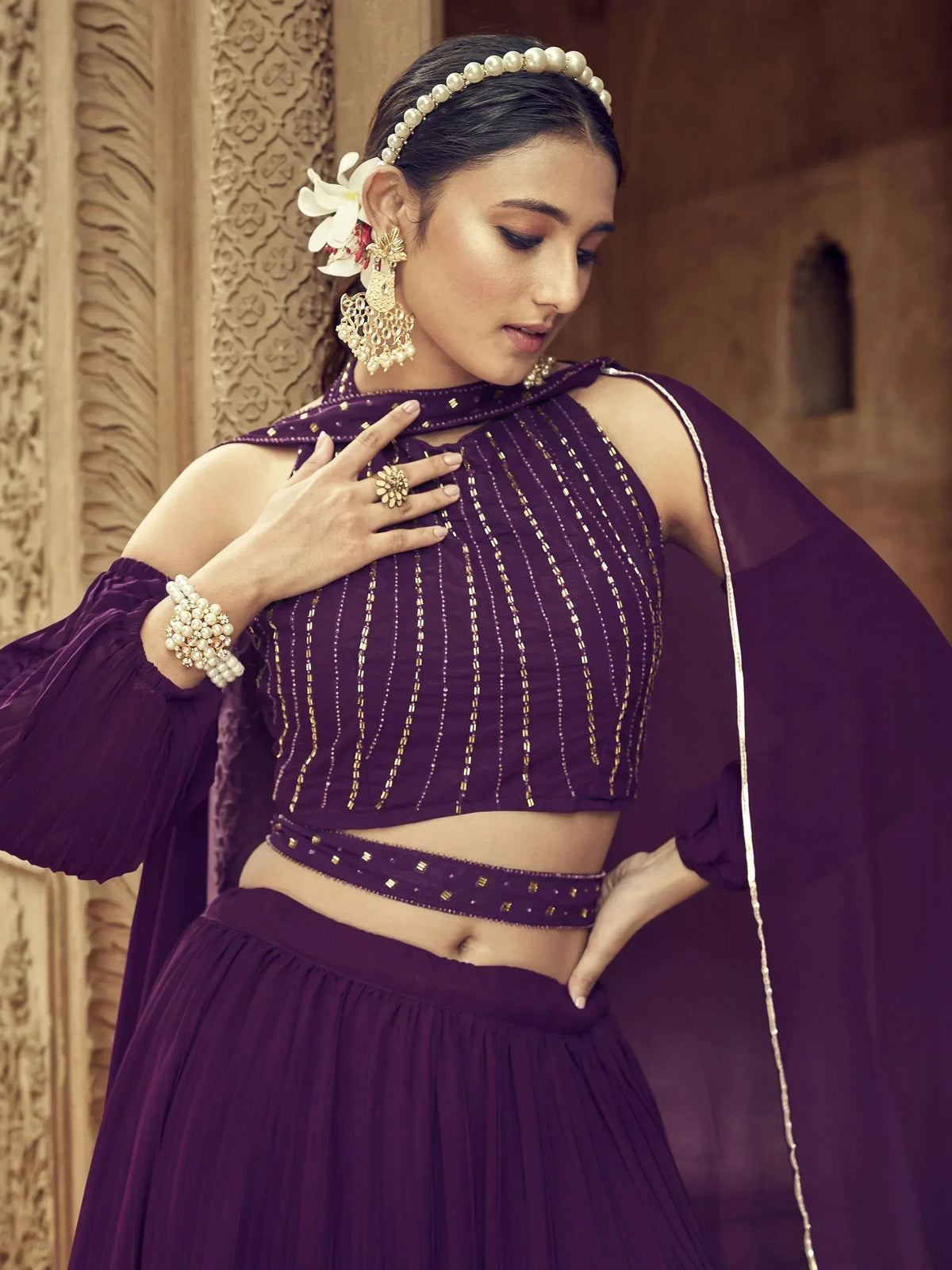 Purple ethnic lehenga choli with gold embroidery, pearl jewelry, and floral hair accessory