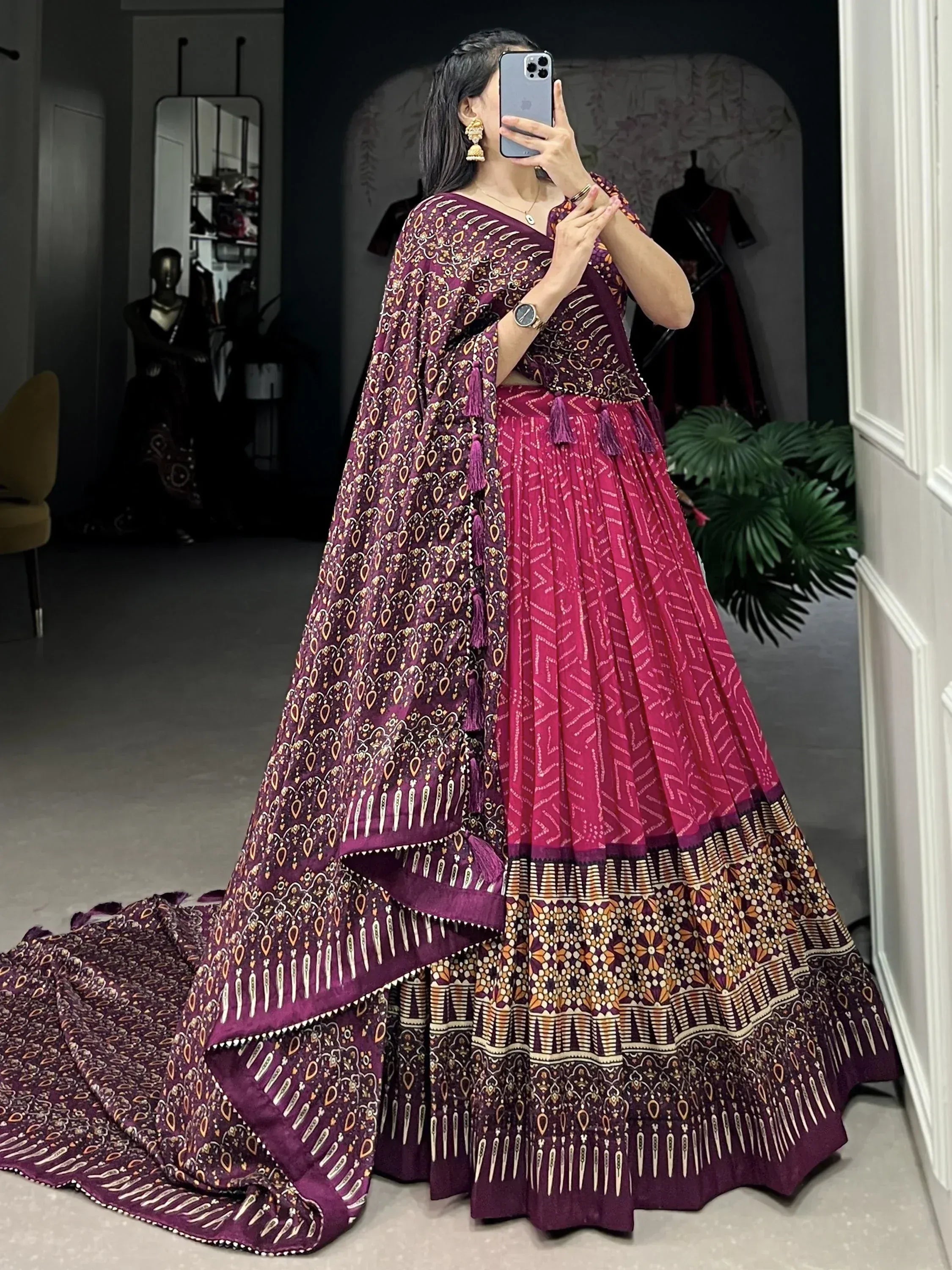Woman in purple and pink printed lehenga choli with tassels, taking mirror selfie in boutique