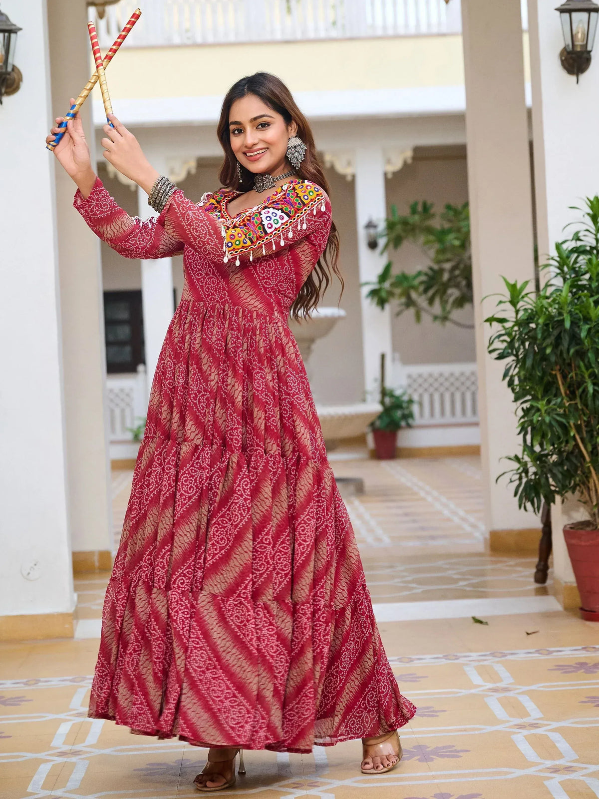 Woman in red ethnic gown with mirror work, holding dandiya sticks, perfect for festive occasions