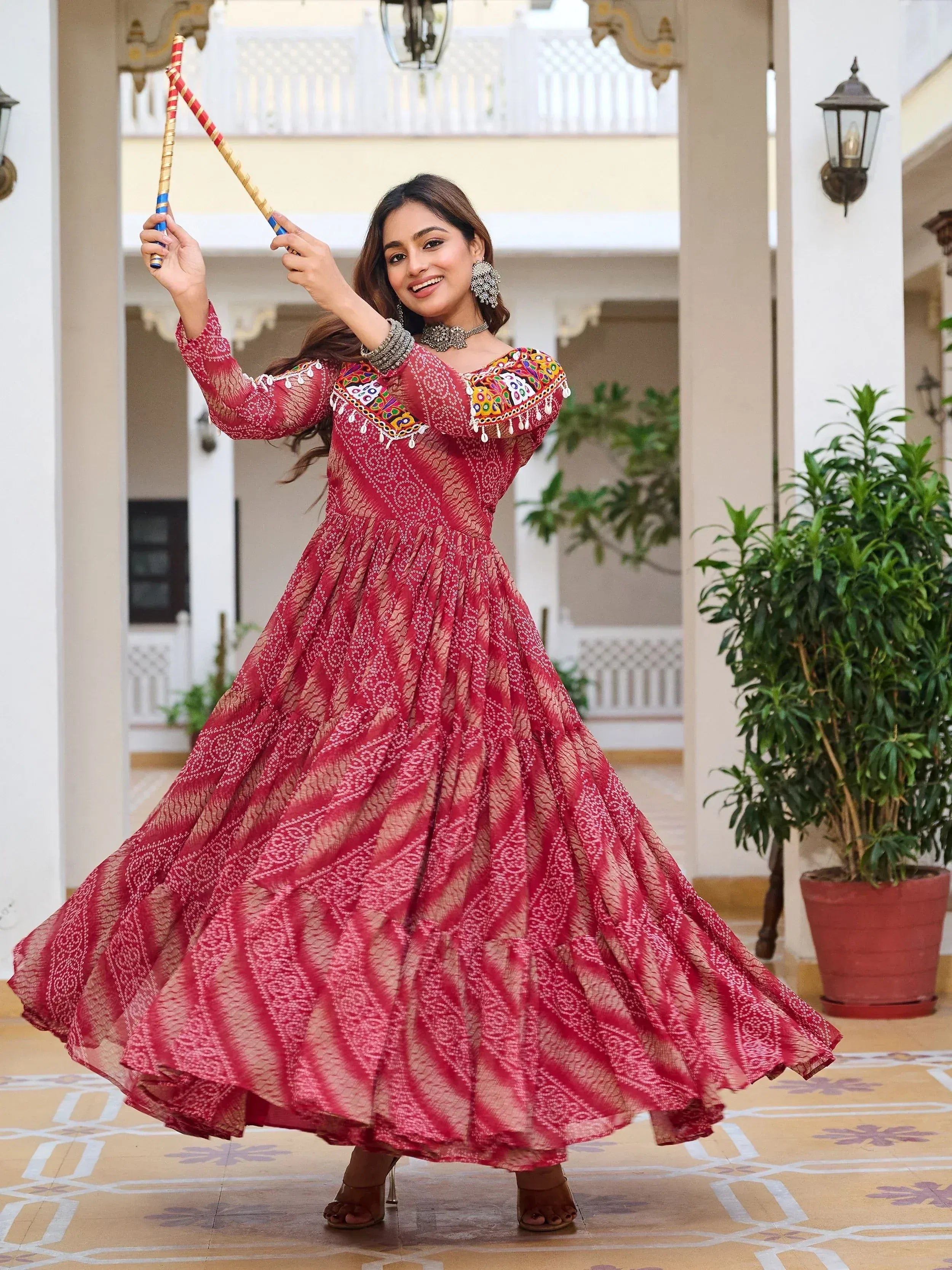Woman in red embroidered ethnic gown dancing with dandiya sticks, perfect for festive occasions.