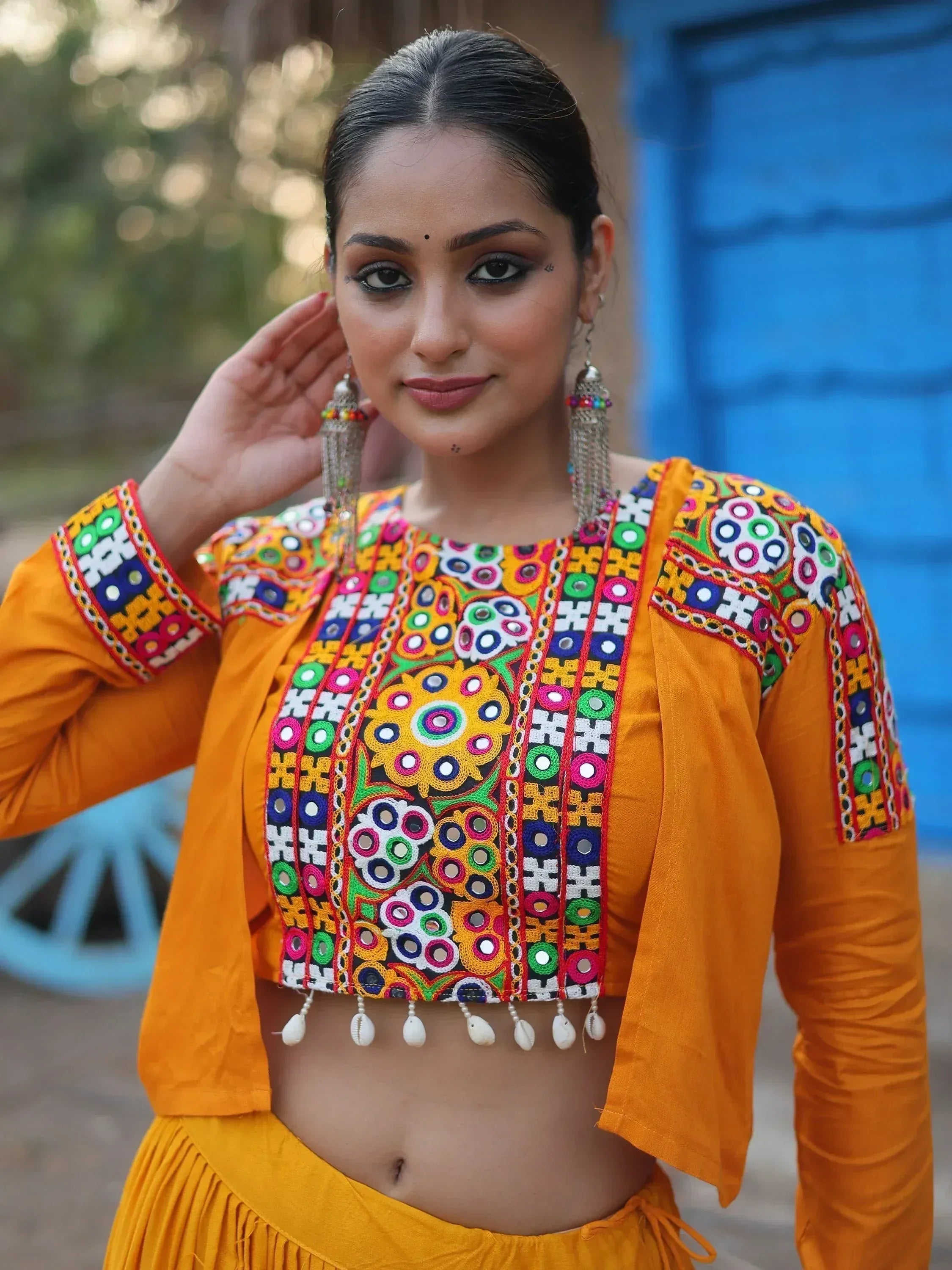 Vibrant yellow ethnic crop top with mirror work and shell tassels, paired with matching skirt for festive occasions