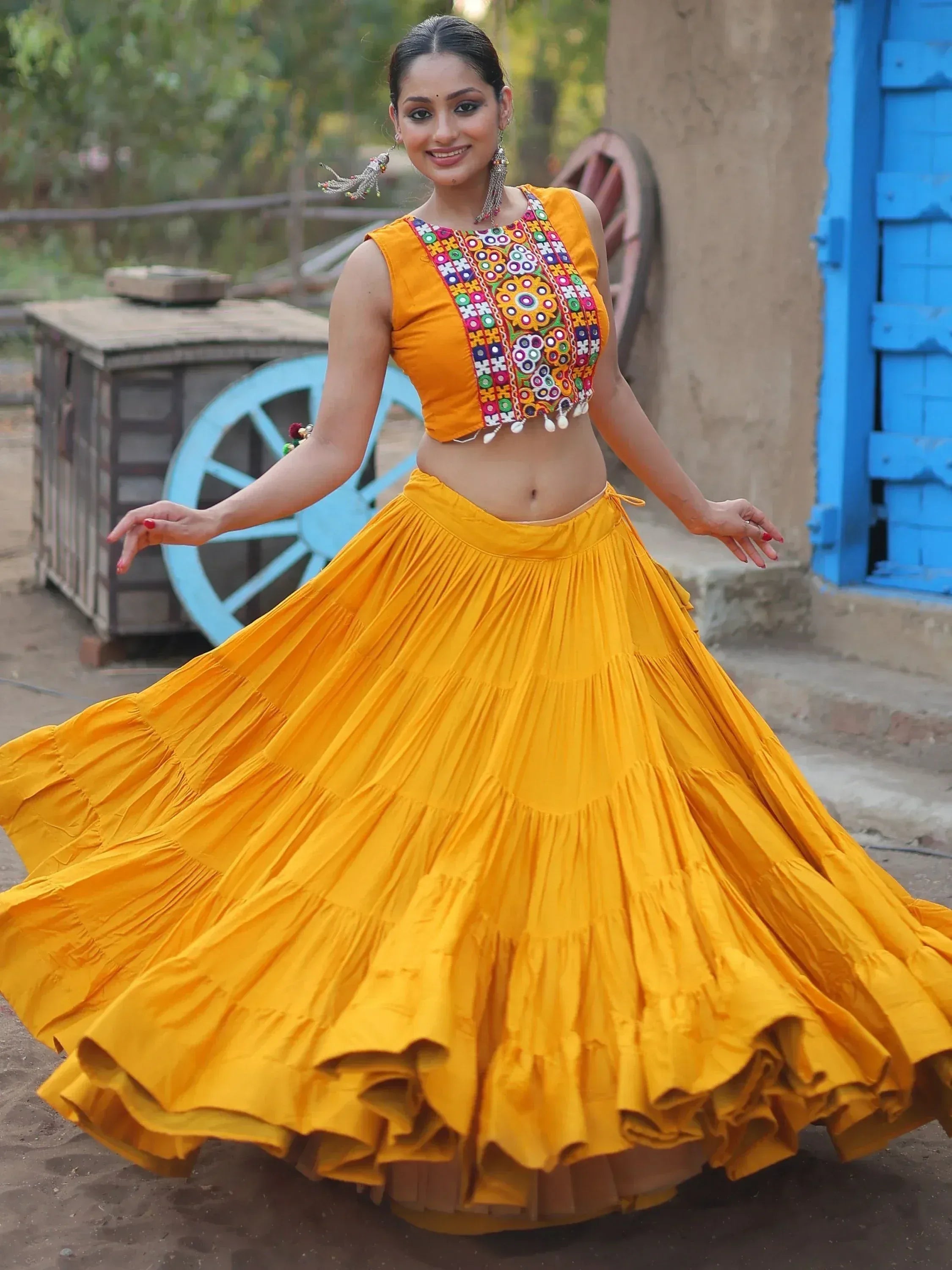 Woman in vibrant yellow ethnic lehenga choli with colorful embroidery, twirling outdoors