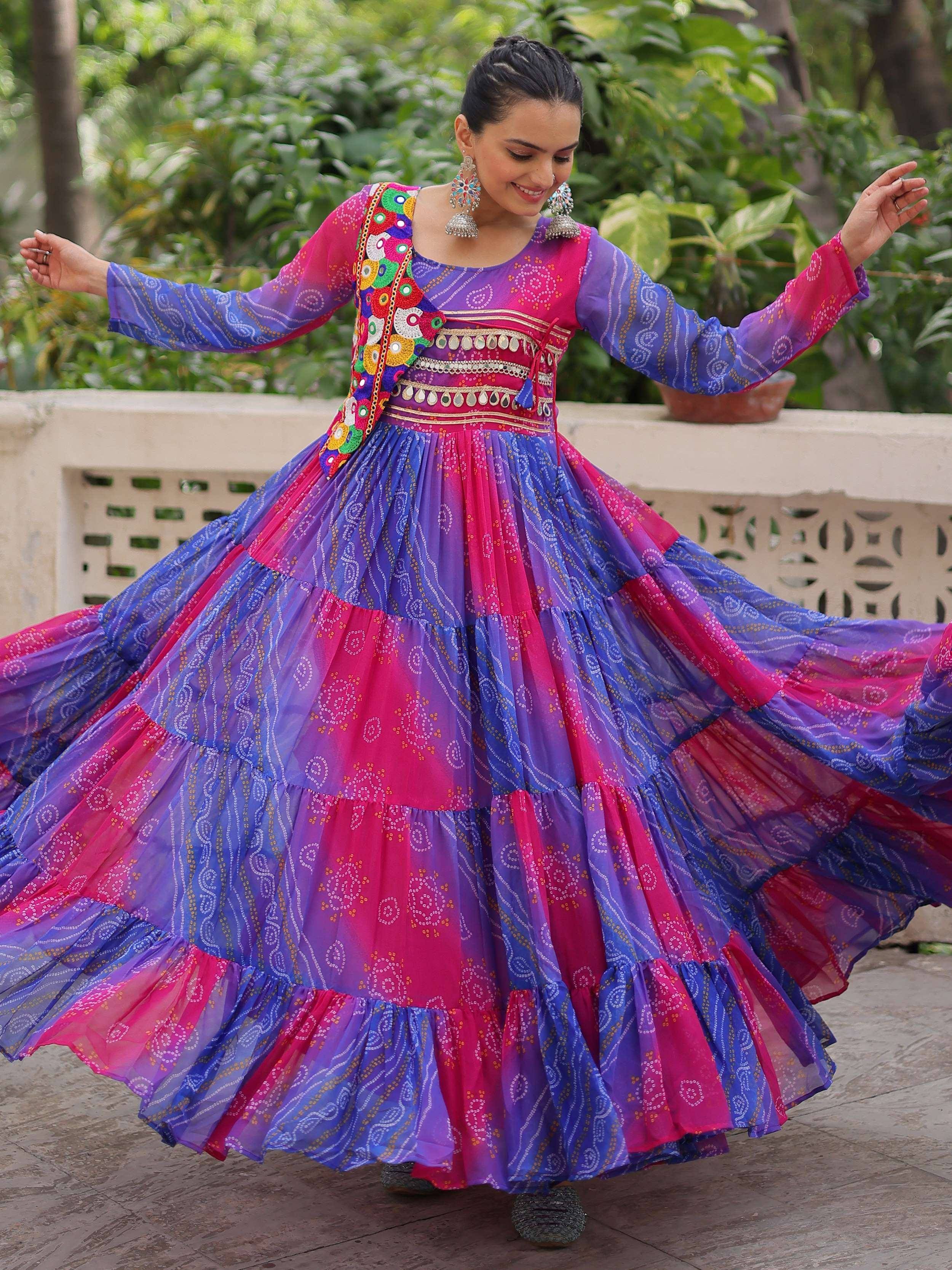 Woman twirling in vibrant Indian ethnic gown with mirror work and tiered skirt, perfect for festive occasions.