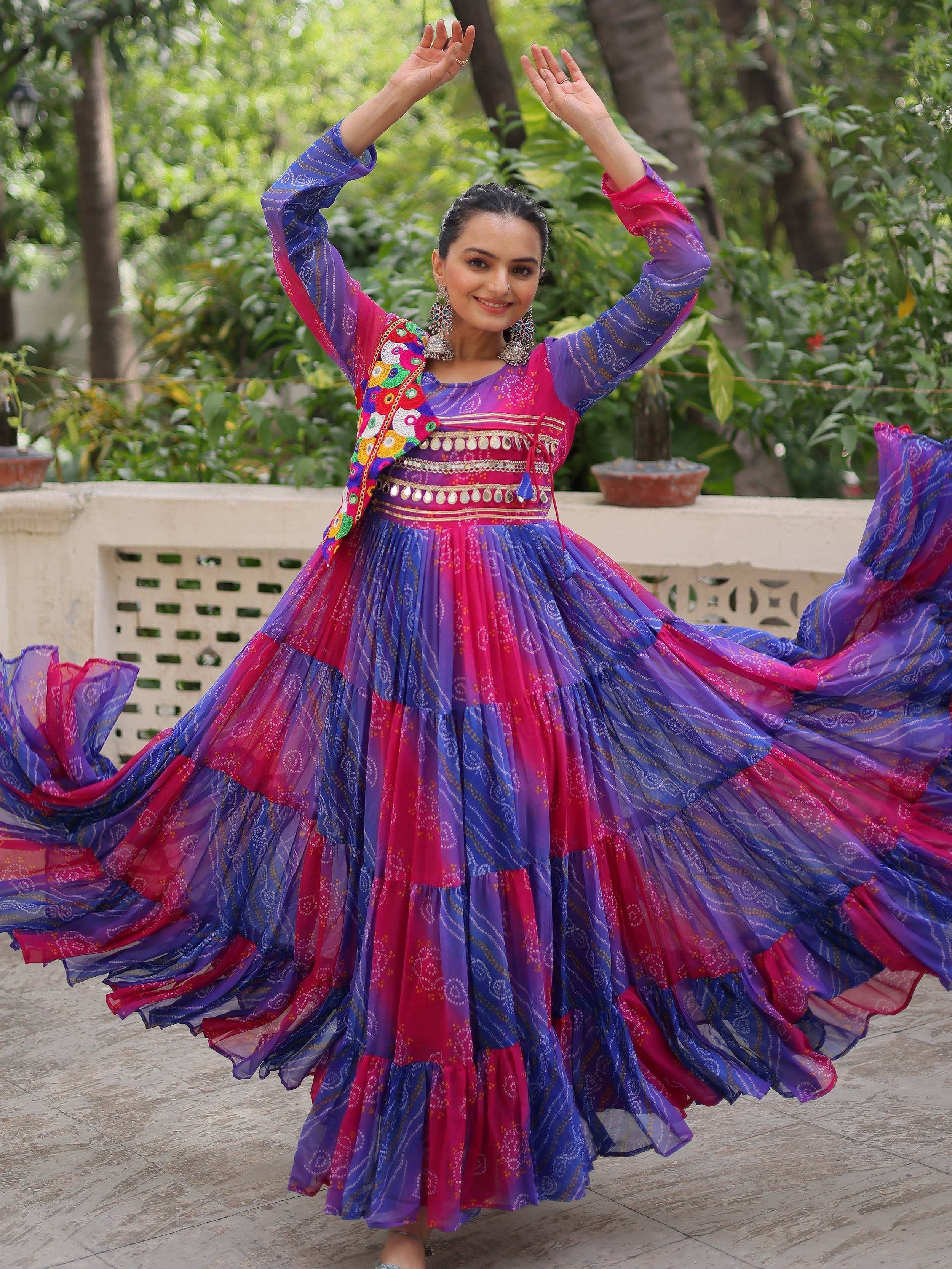 Woman dancing in vibrant purple and pink ethnic gown with mirror work, perfect for festive occasions.