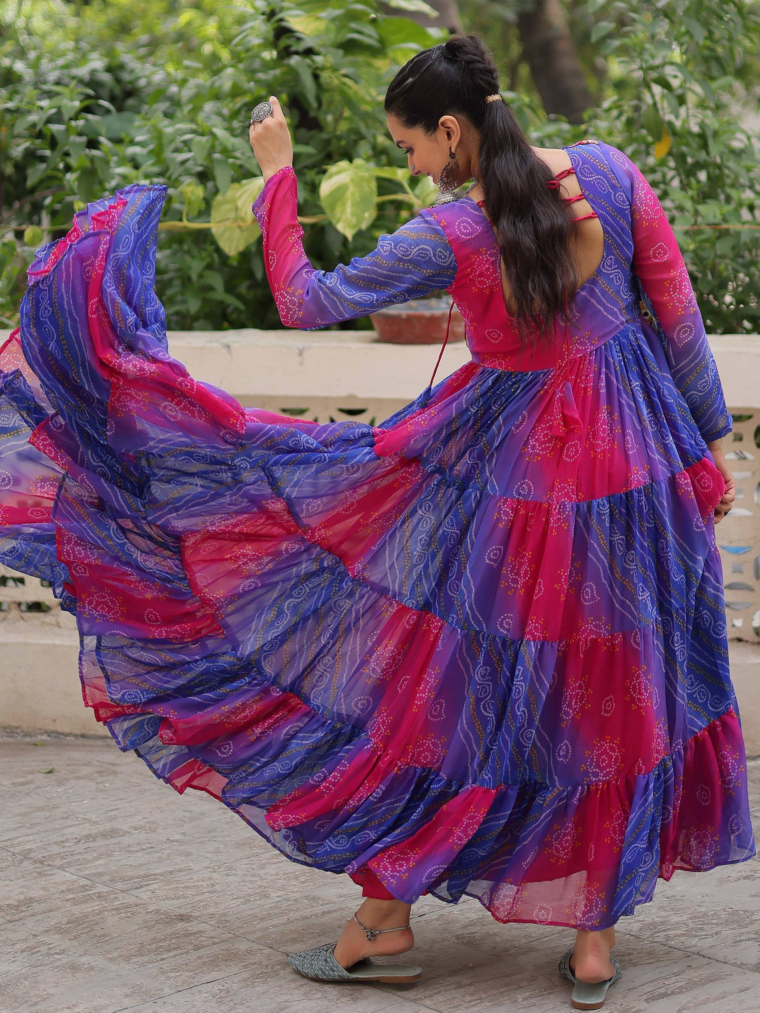 Woman twirling in vibrant pink and blue tiered ethnic gown with printed patterns, perfect for festive occasions.