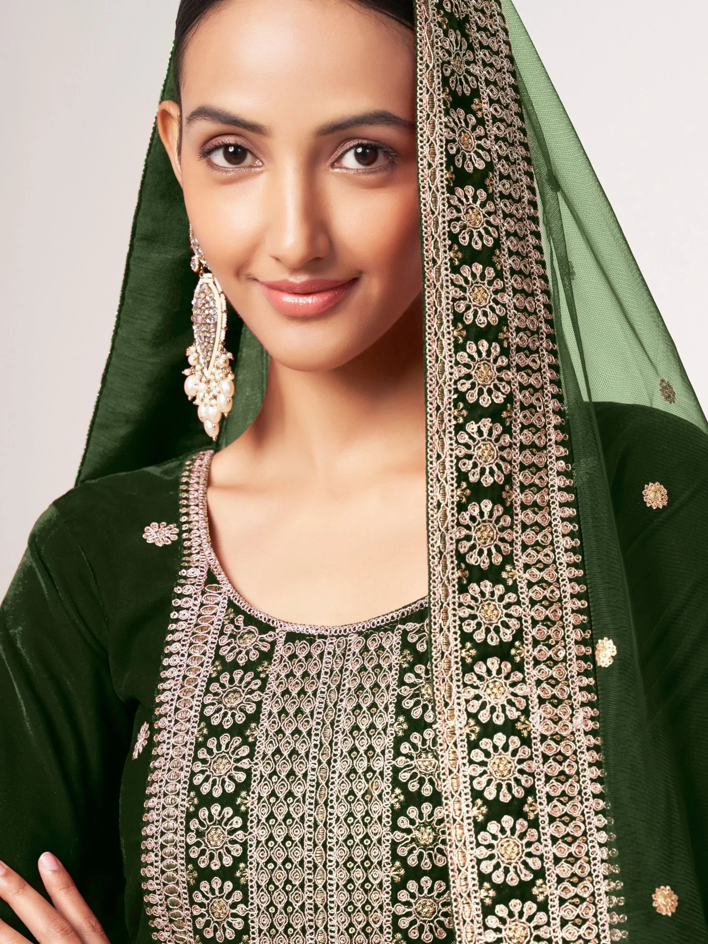 Woman in dark green embroidered salwar kameez with matching dupatta and statement earrings