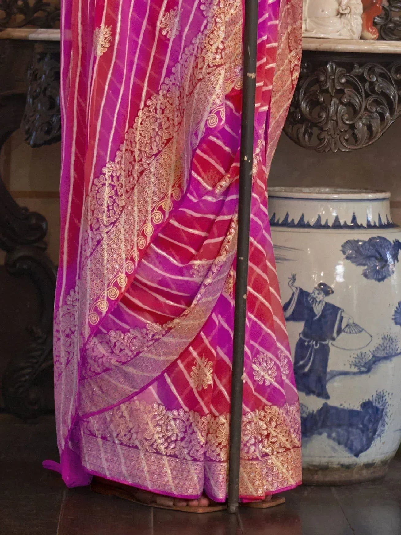 Pink and gold embroidered saree with intricate floral patterns, displayed on mannequin near decorative vase