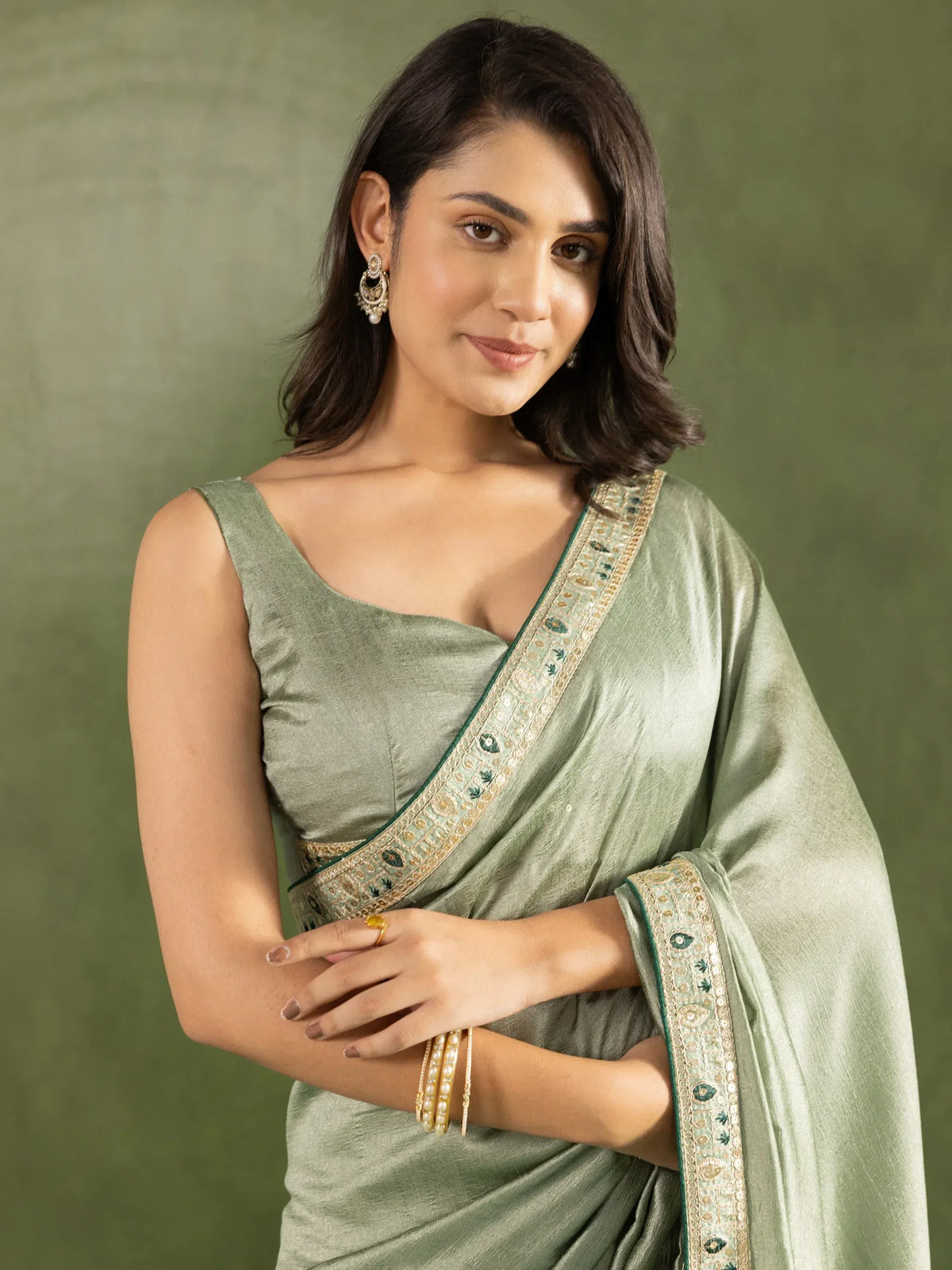 Elegant olive green saree with gold and green embroidered border, paired with statement earrings and bangles