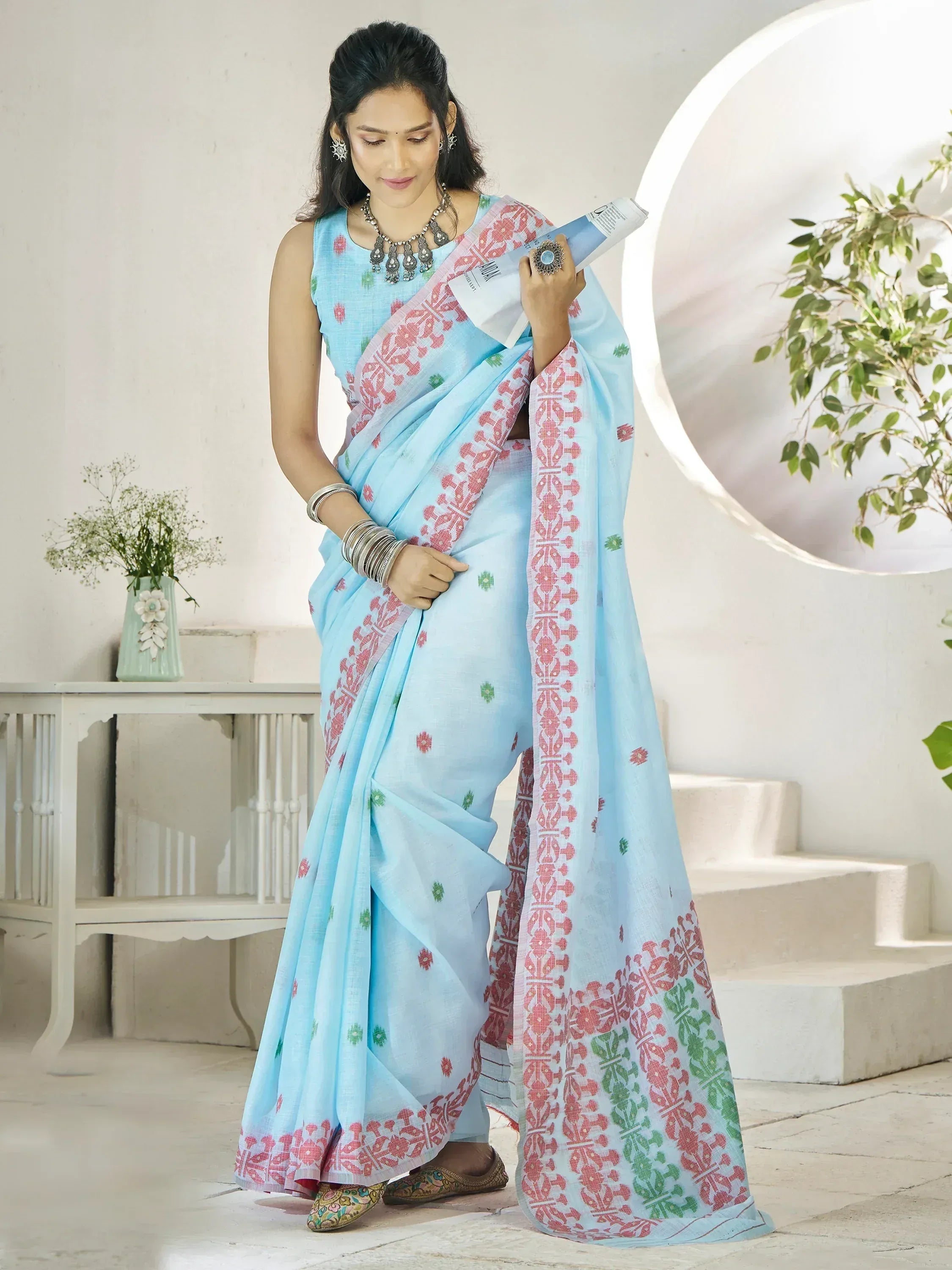 Light blue saree with red and green block print, paired with sleeveless blouse and traditional jewelry