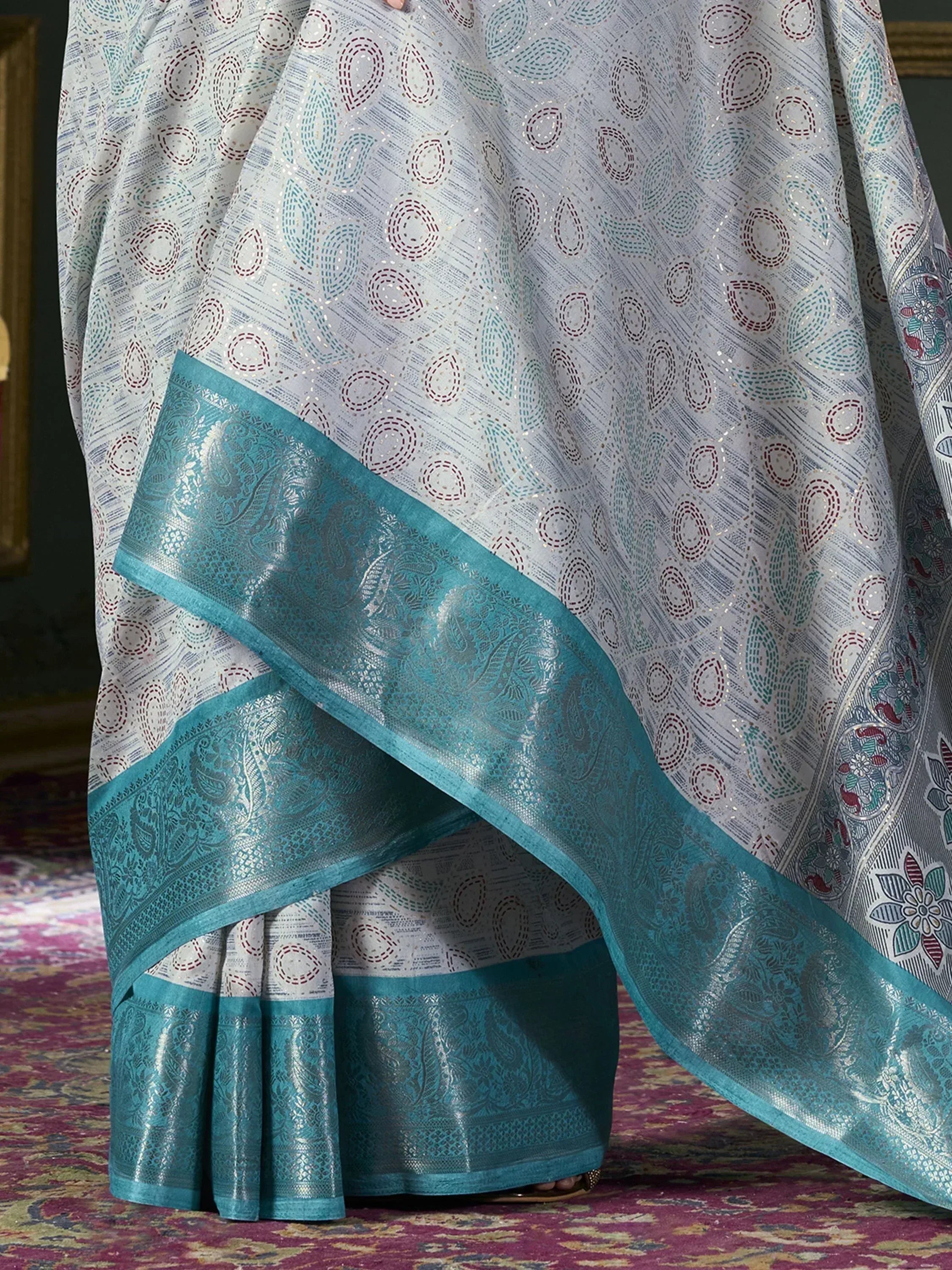 White and teal designer saree with intricate paisley border and embroidered motifs, perfect for ethnic occasions.