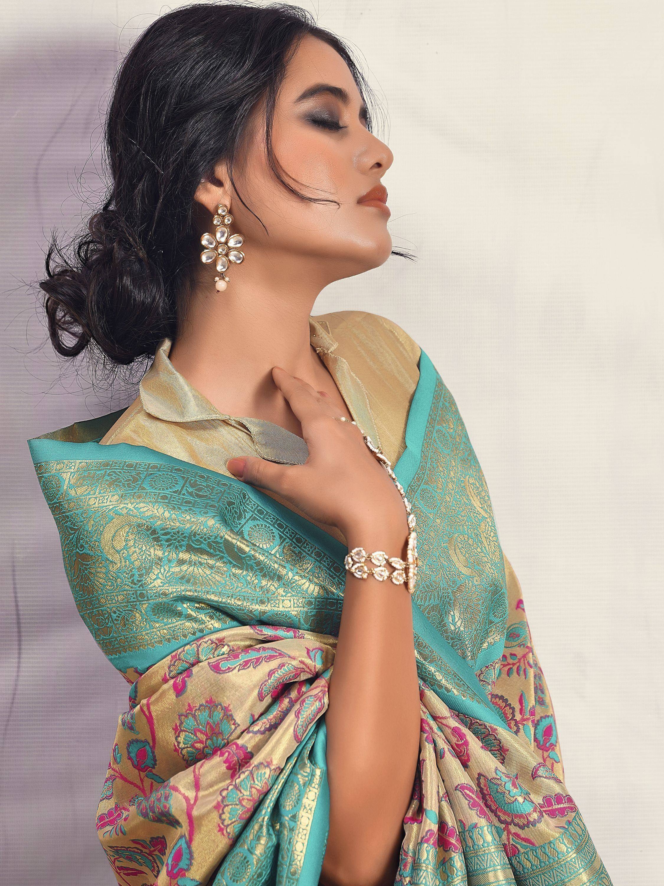 Woman in elegant turquoise and gold designer saree with floral patterns, paired with pearl jewelry