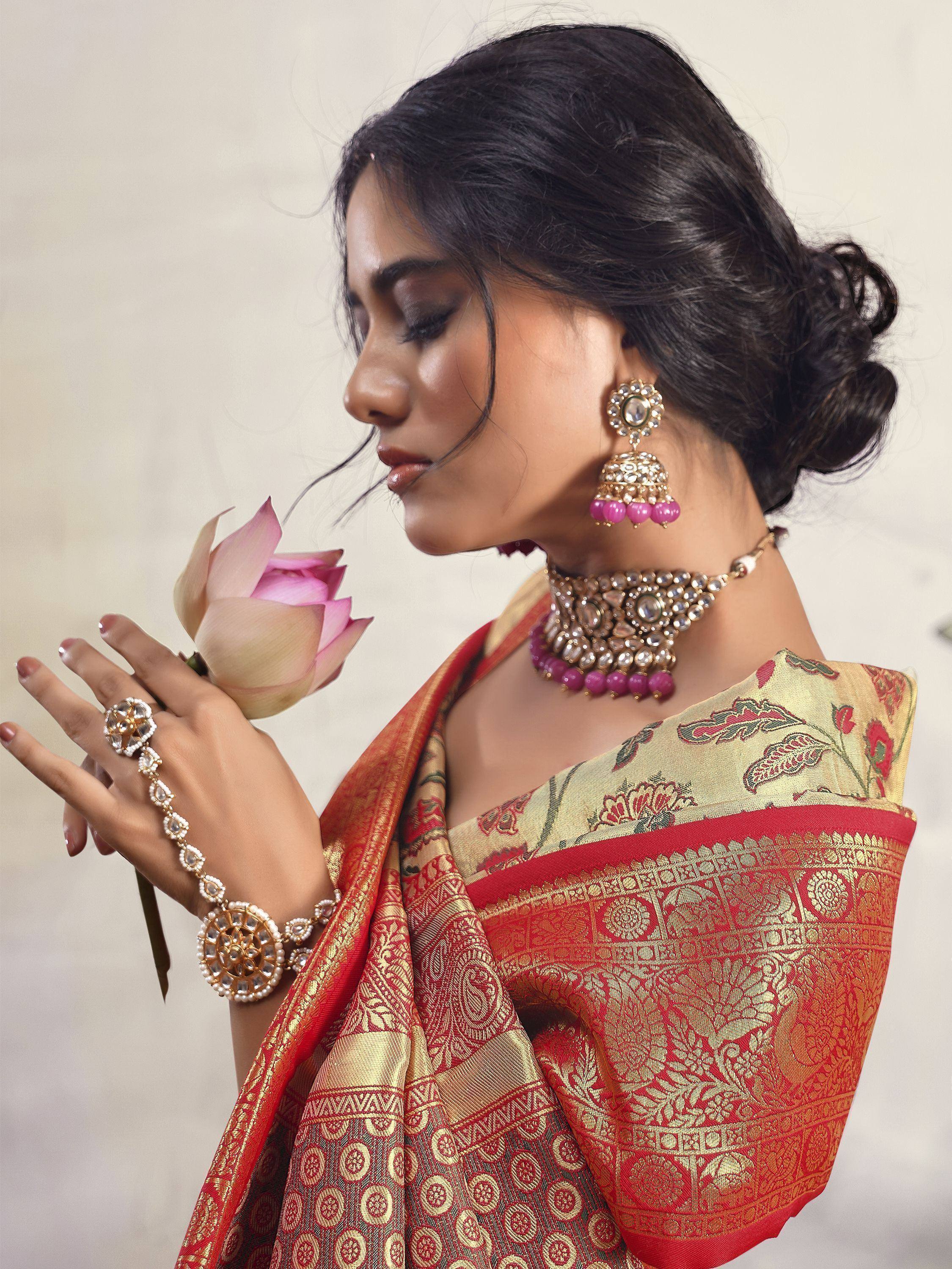 Woman in red and gold embroidered saree with traditional jewelry holding pink lotus flower