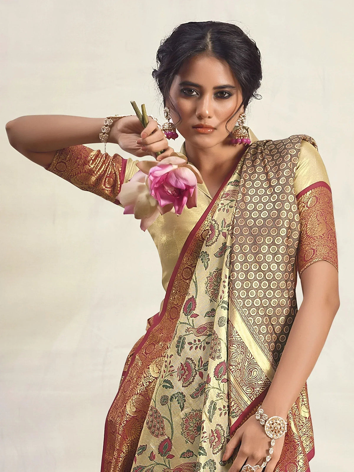 Woman in elegant gold and maroon printed saree with floral design, holding pink lotus flower