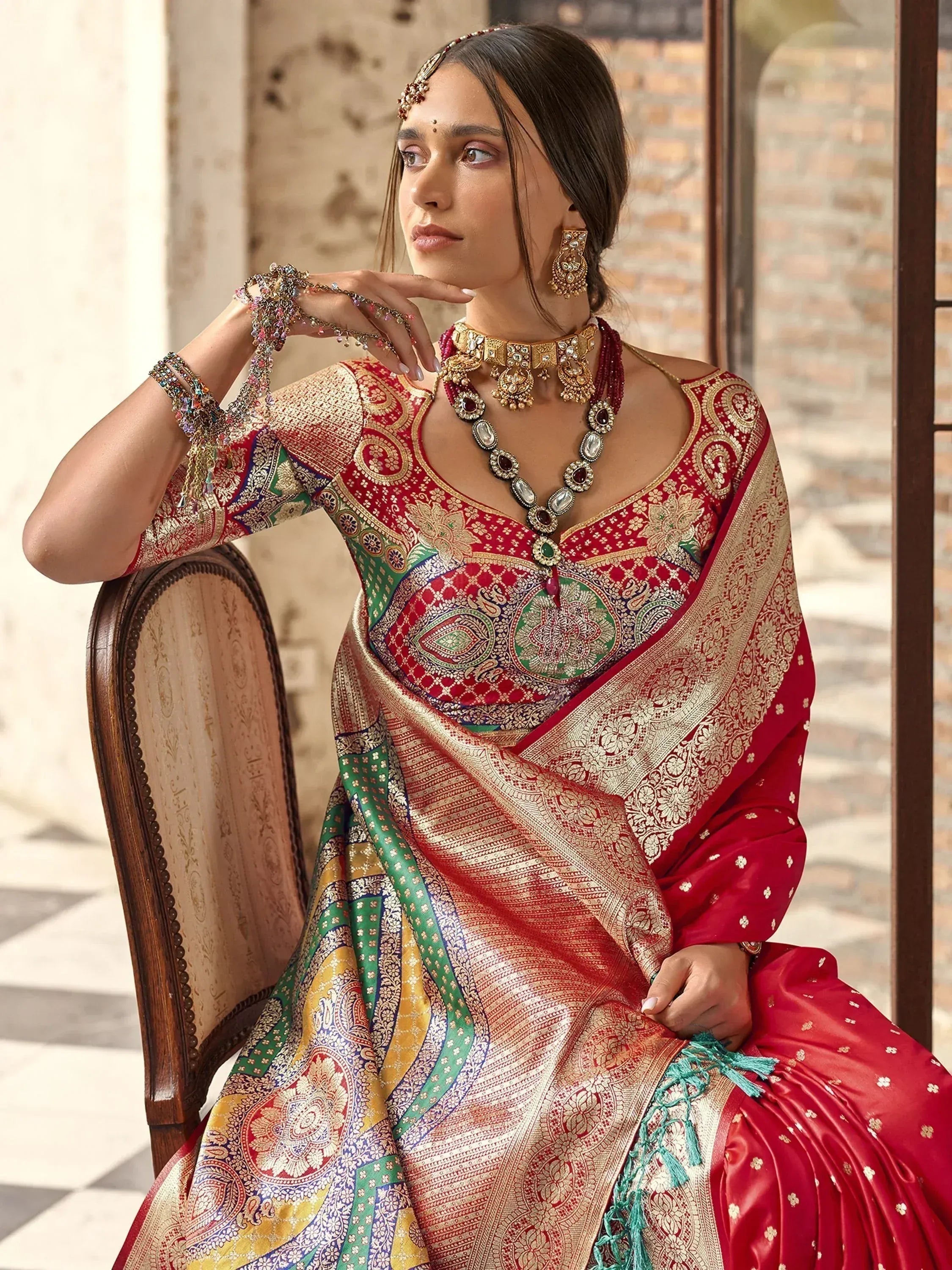 Woman in red and gold embroidered saree with traditional Indian jewelry, seated elegantly