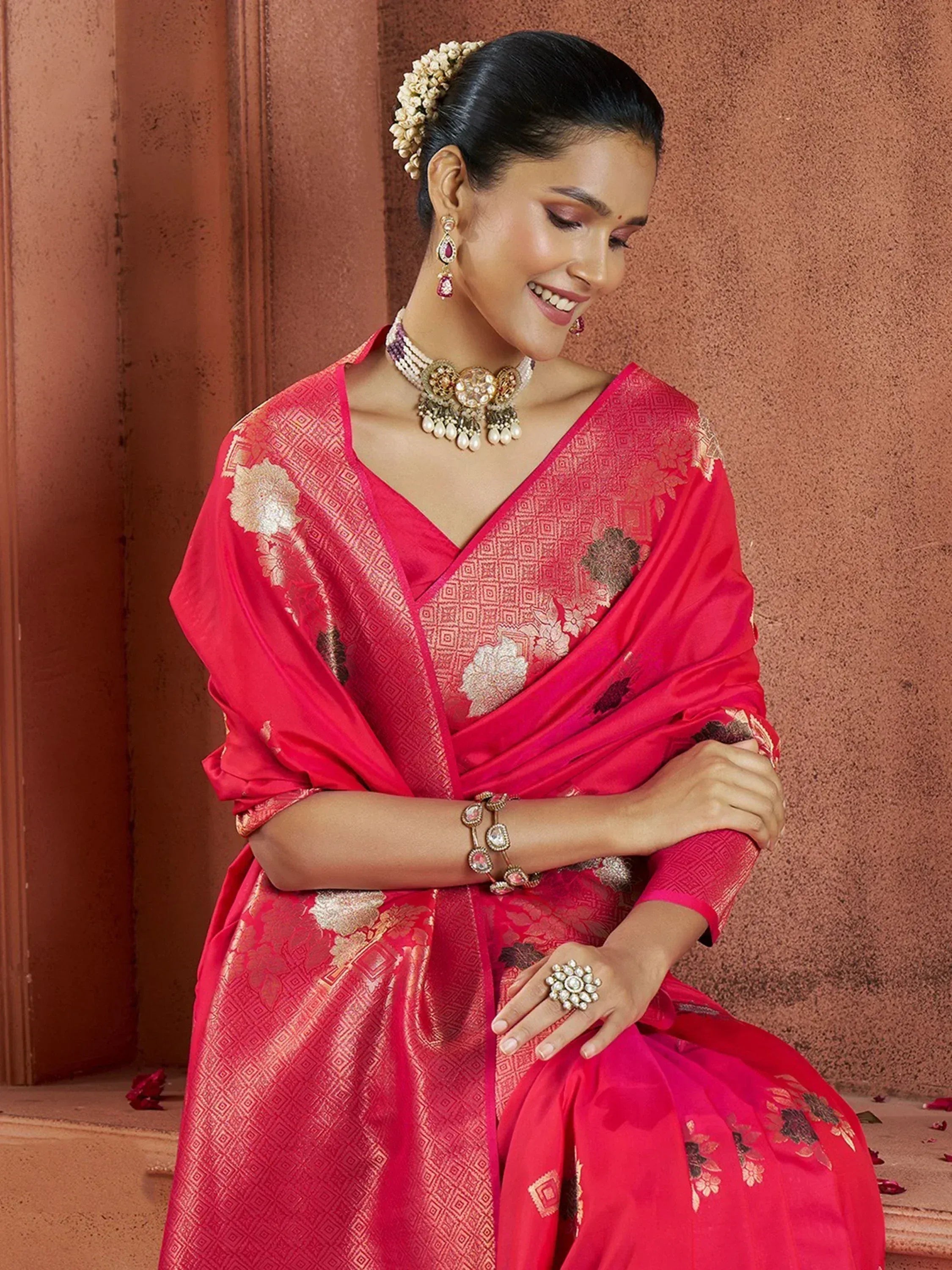 Woman in vibrant pink ethnic saree with gold floral embroidery, traditional jewelry, and floral hair accessory