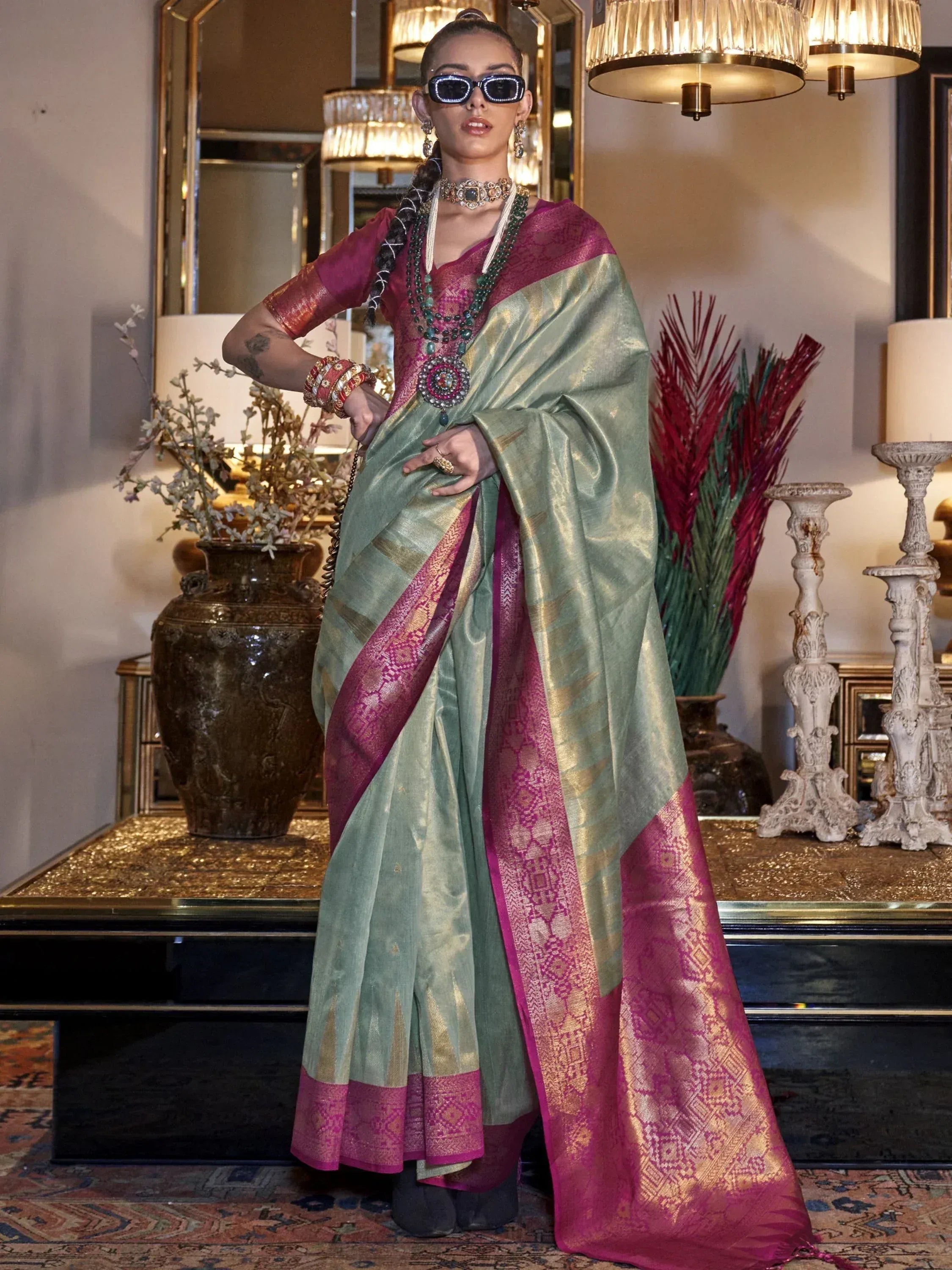 Stylish woman in green and pink designer saree with gold border, ethnic jewelry, and sunglasses