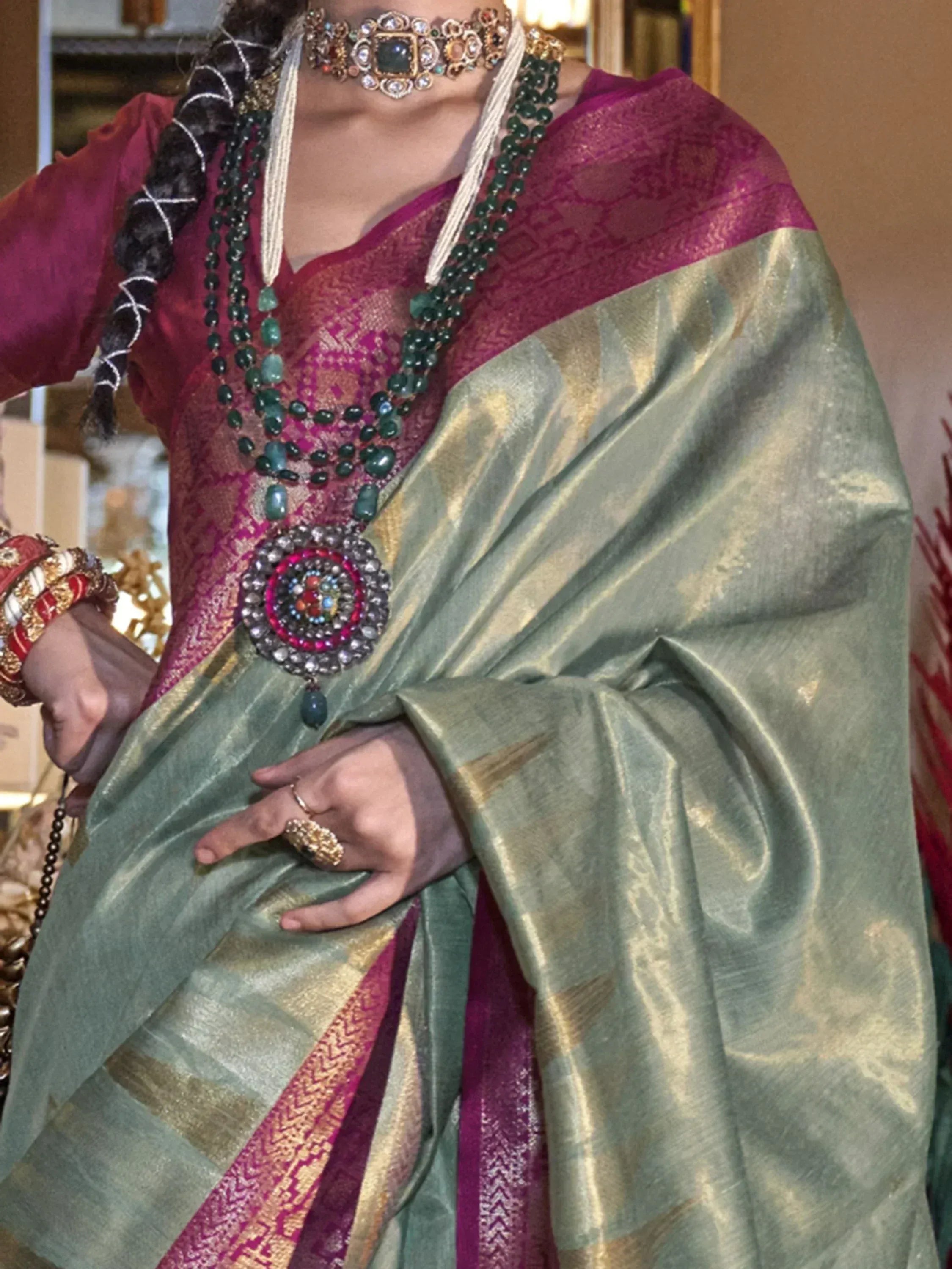 Woman in elegant Indian saree with green and magenta hues, adorned with traditional jewelry and intricate embroidery.