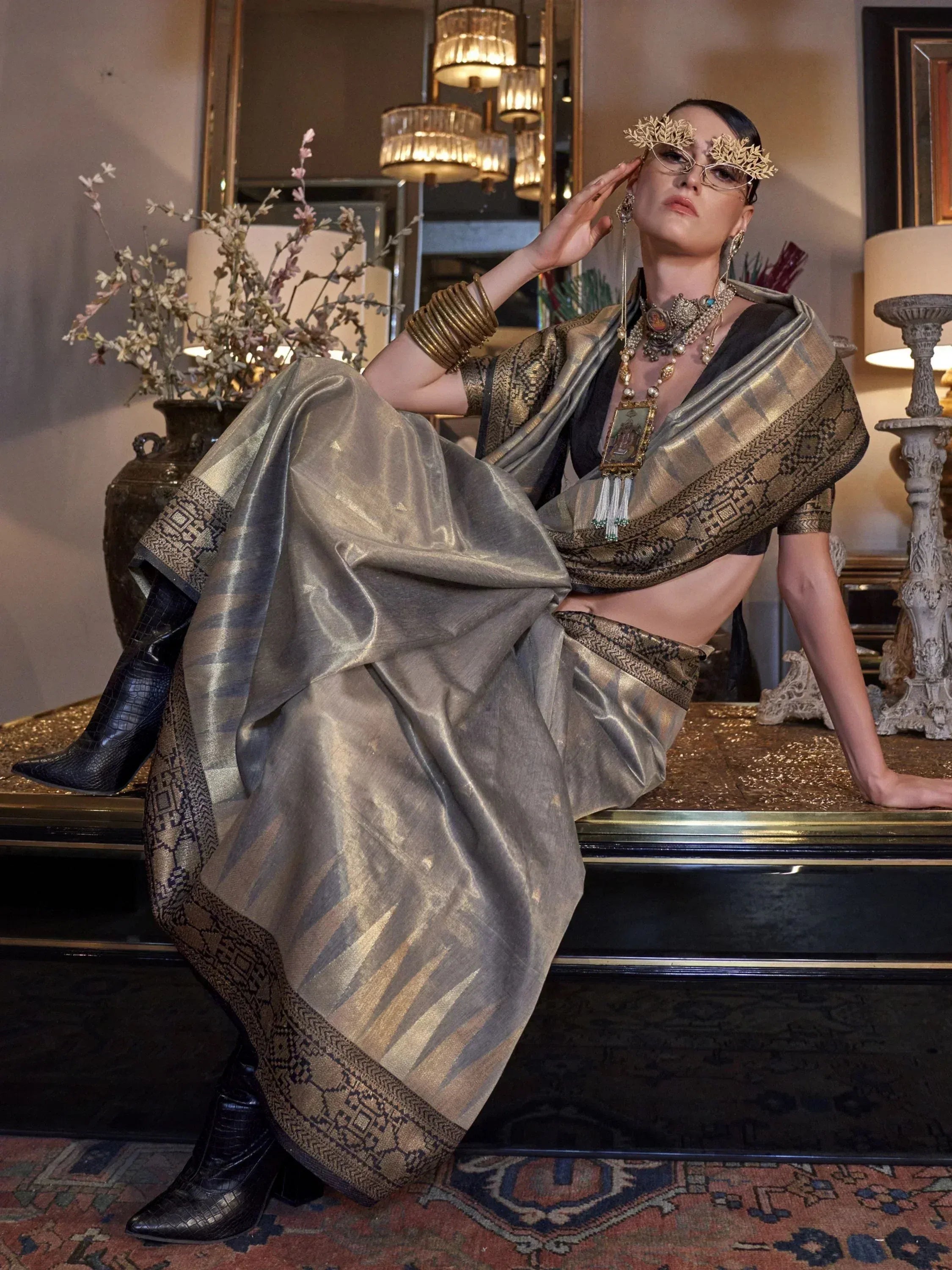 Elegant woman in designer saree with gold embroidery, statement jewelry, and black boots, styled for ethnic fashion.