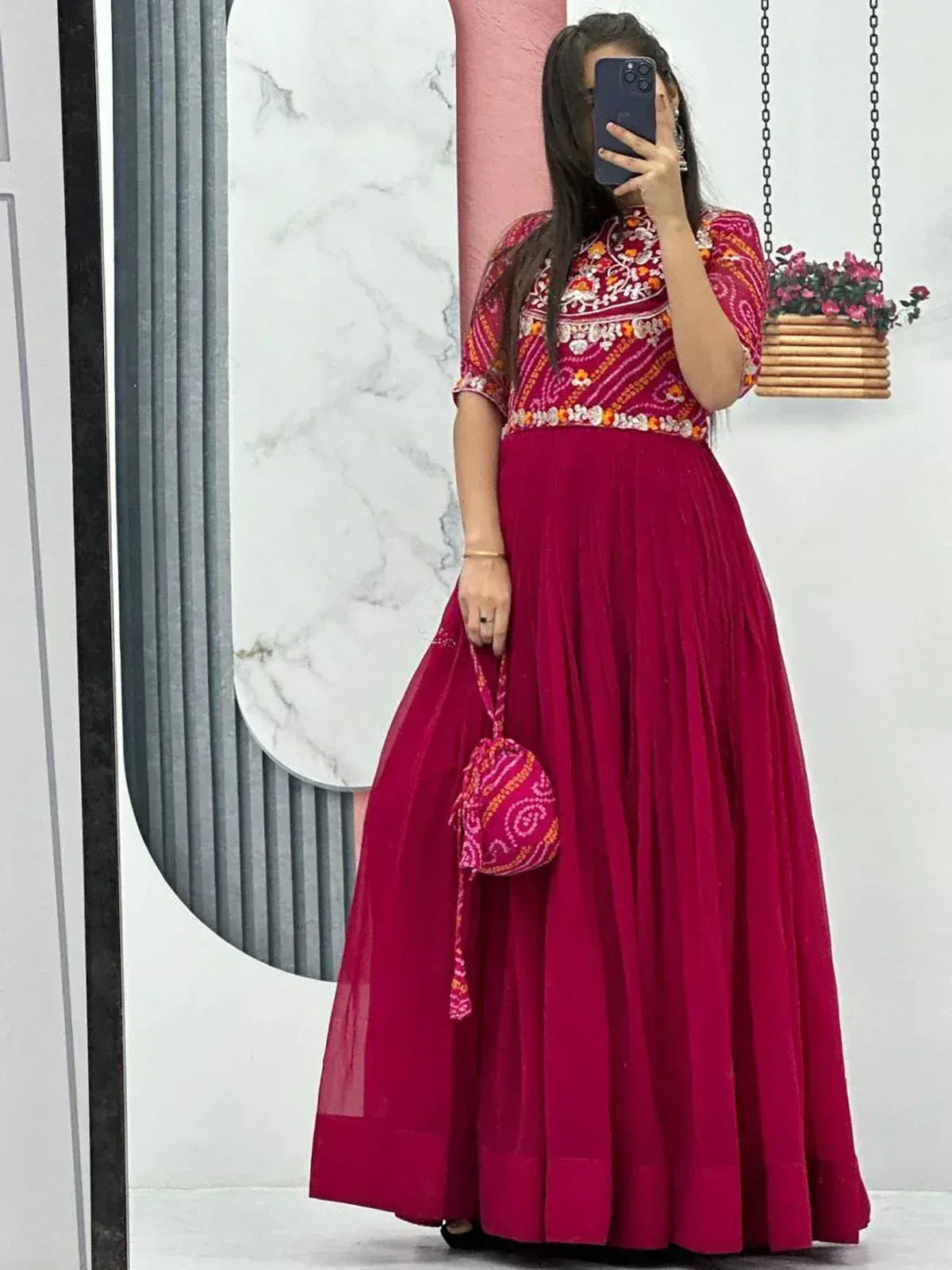 Vibrant maroon ethnic gown with floral embroidery and matching potli bag for festive occasions