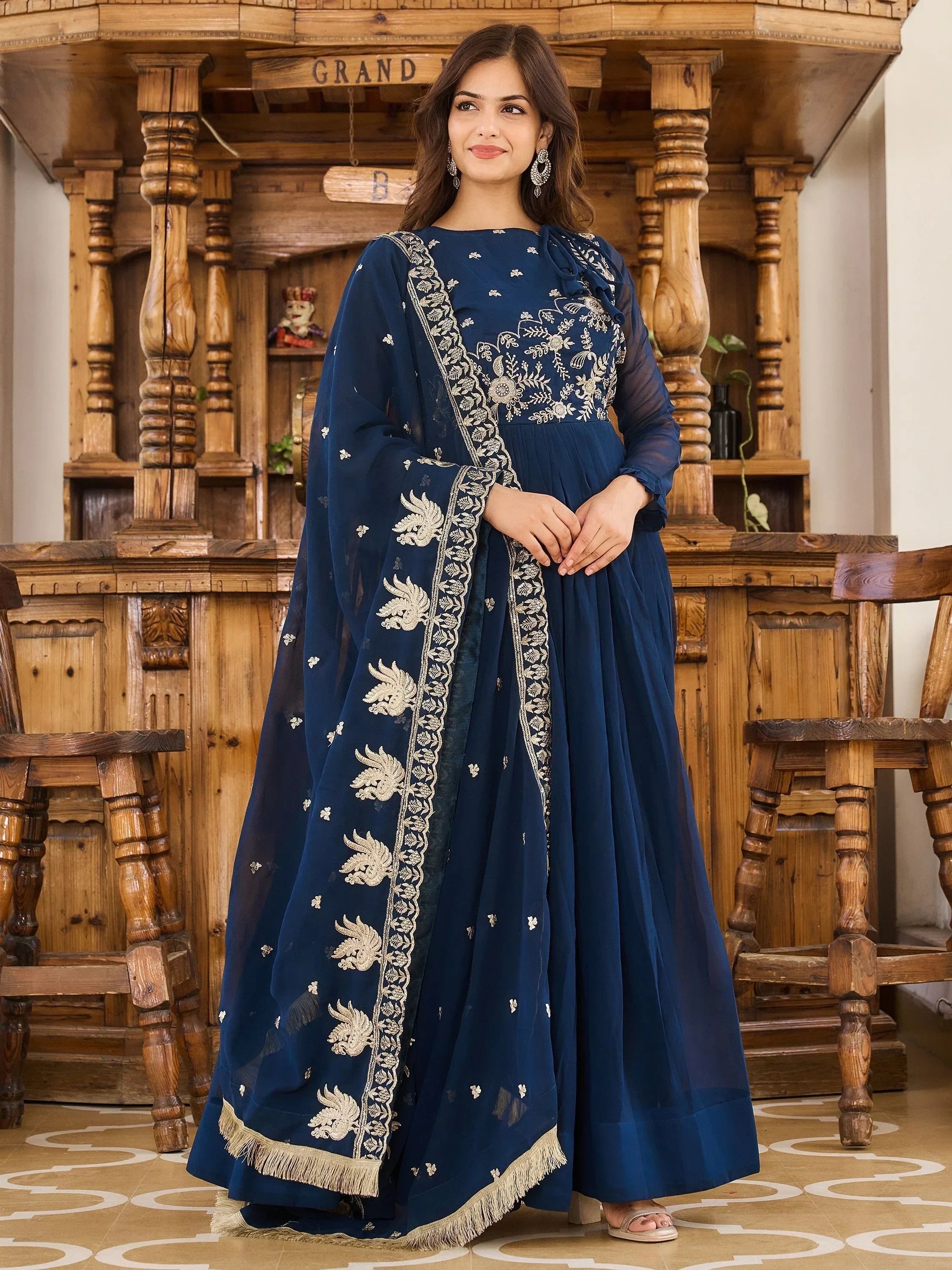 Woman wearing navy blue embroidered ethnic gown with matching dupatta in wooden interior