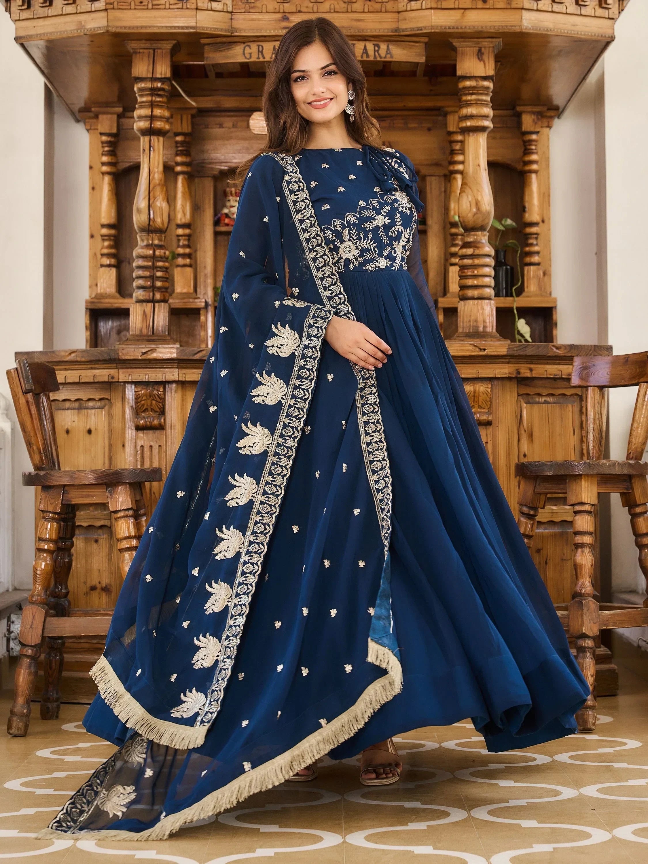 Woman in a royal blue embroidered ethnic gown with dupatta, standing indoors