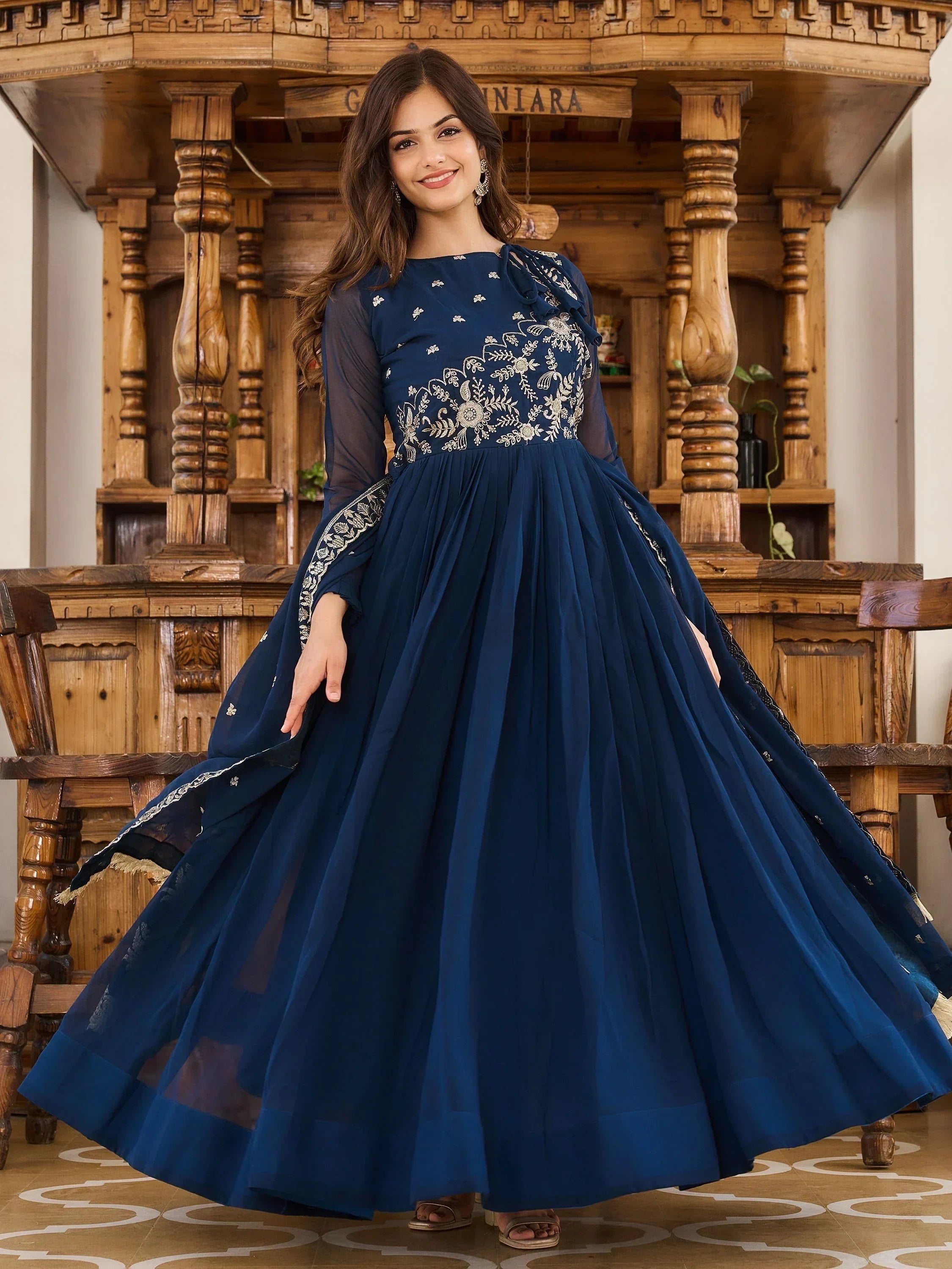 Woman wearing a navy blue embroidered Indian ethnic gown with sheer sleeves indoors
