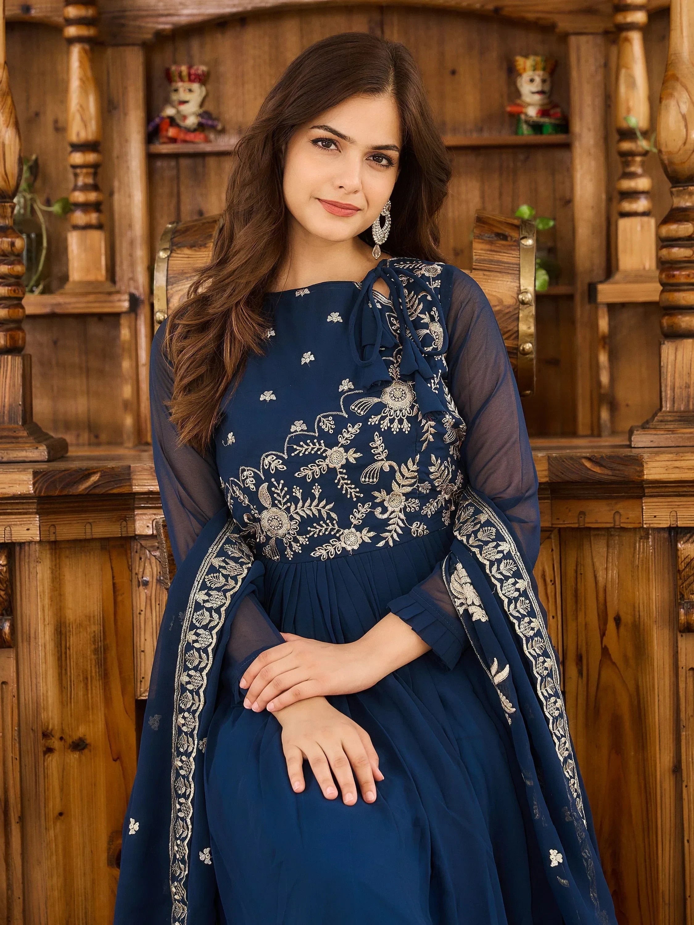Woman in blue embroidered ethnic gown with sheer sleeves, sitting indoors
