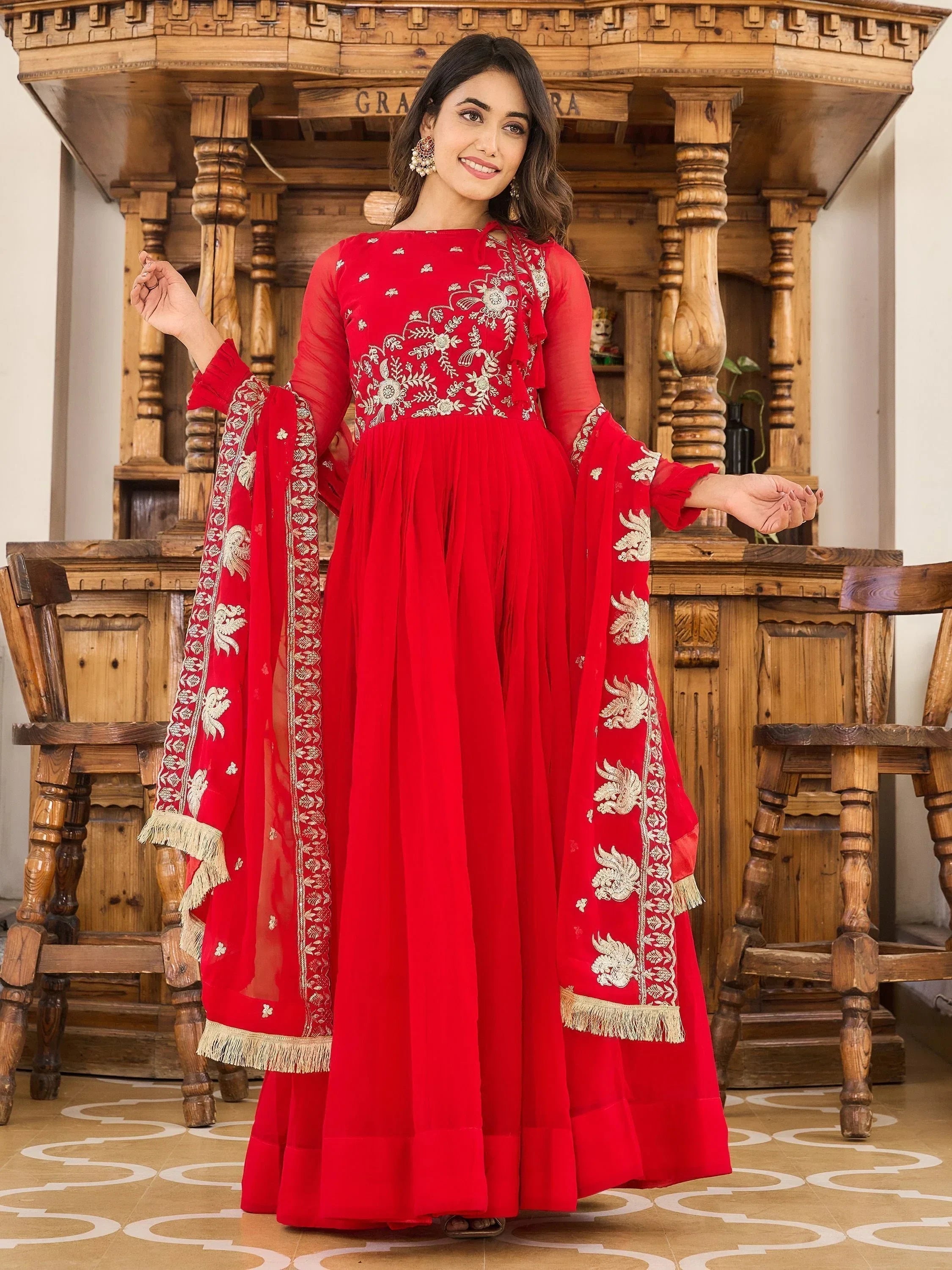 Woman wearing red embroidered anarkali suit with dupatta in ethnic setting