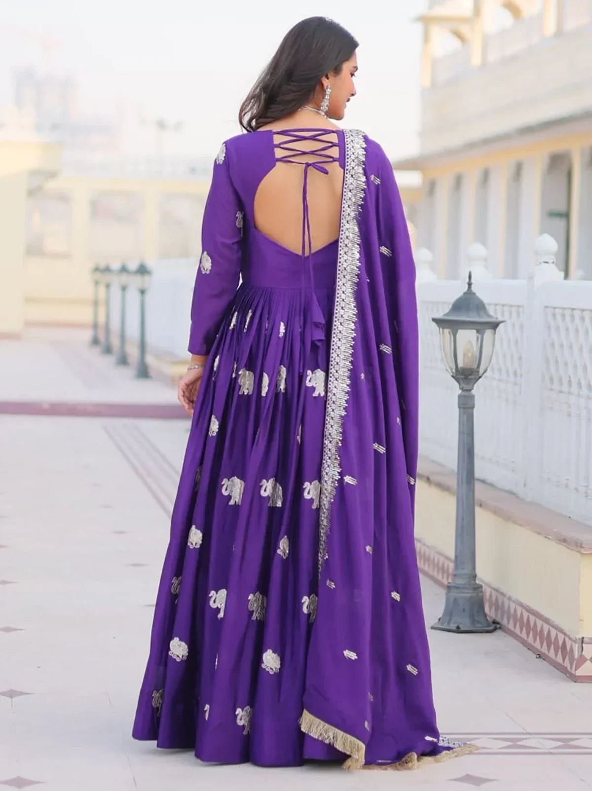 Woman wearing purple embroidered ethnic gown with open-back design and silver dupatta