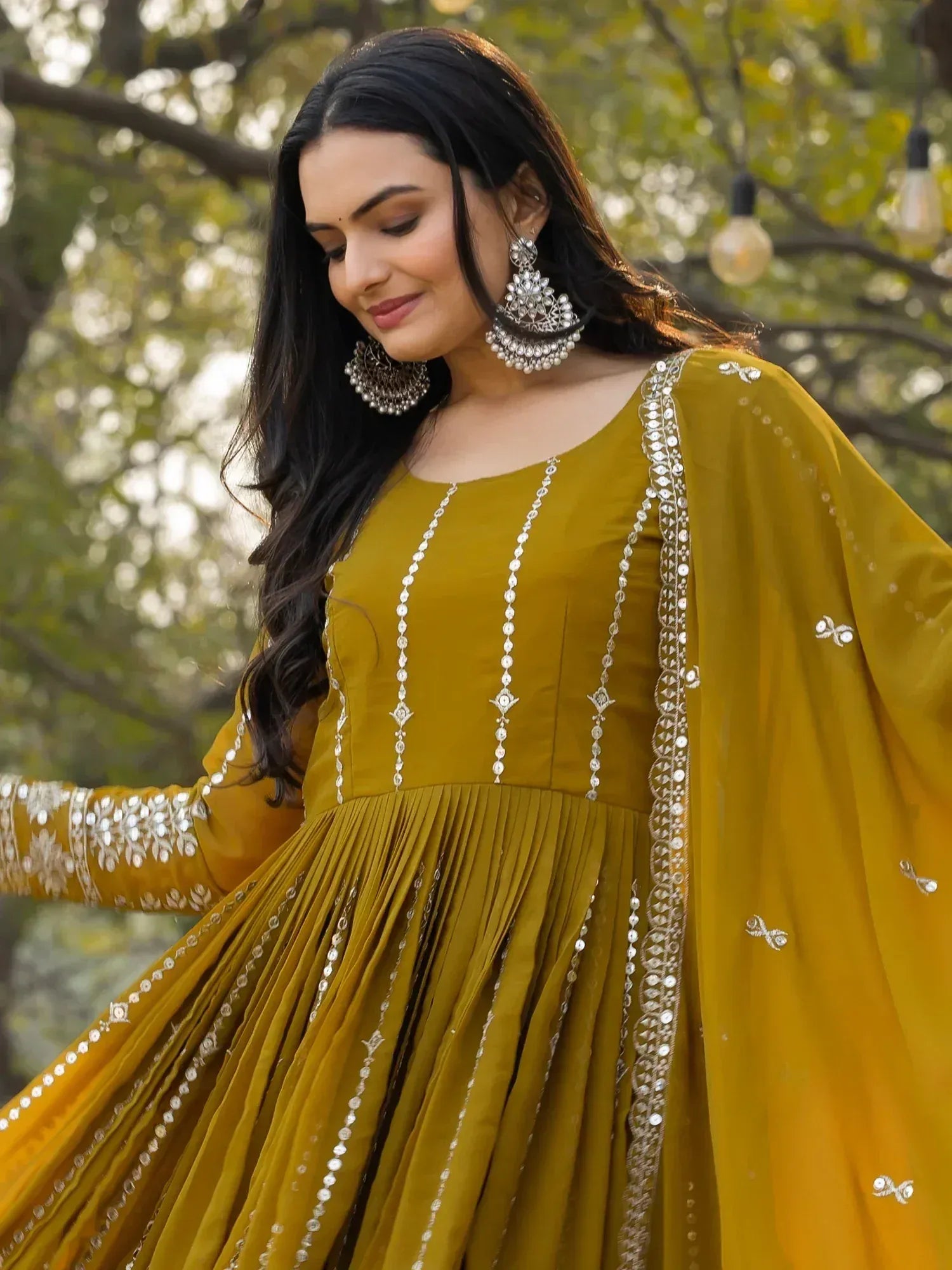 Mustard yellow ethnic gown with silver mirror work, pleated skirt, and statement earrings for festive occasions