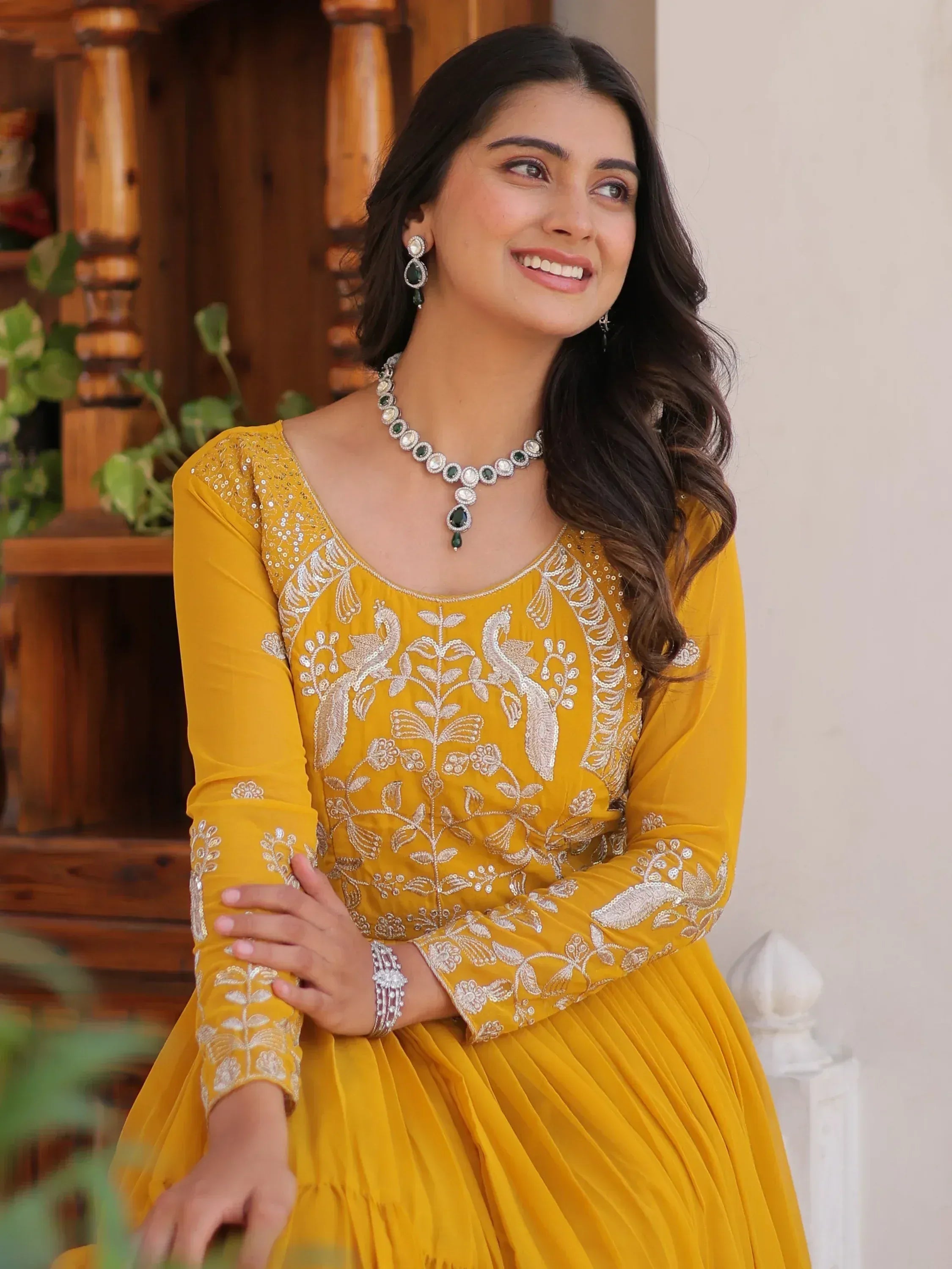 Yellow embroidered ethnic gown with peacock design, paired with green stone jewelry for Indian wear