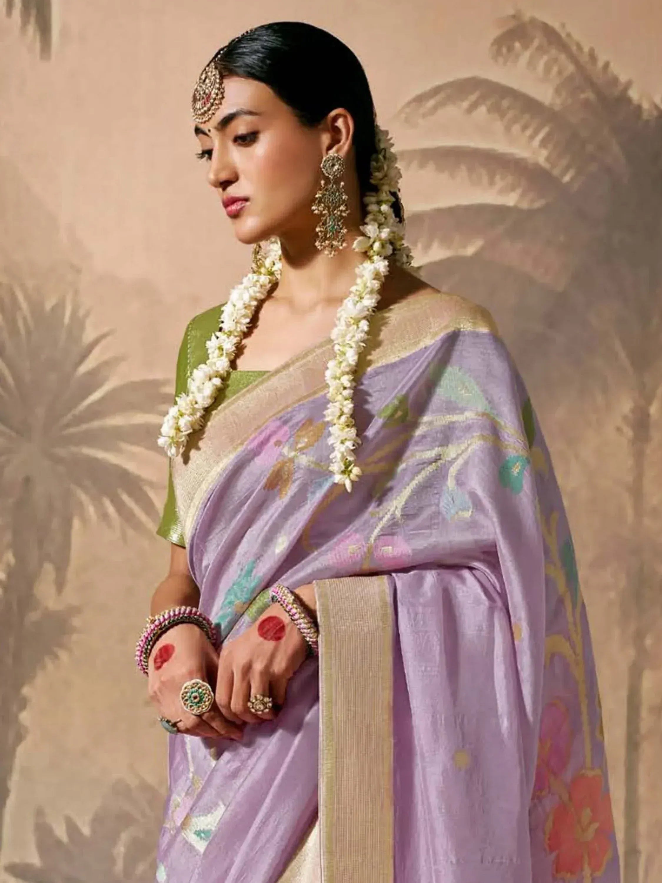 Woman in lavender floral saree with green blouse, traditional jewelry, and jasmine garland