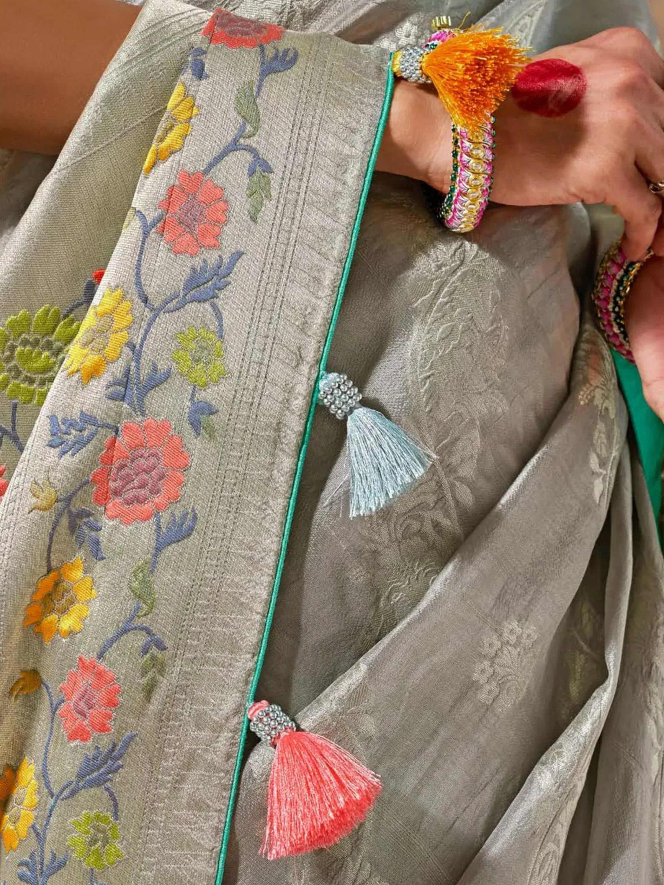 Grey floral embroidered saree with colorful tassels and traditional bangles, perfect for ethnic occasions.