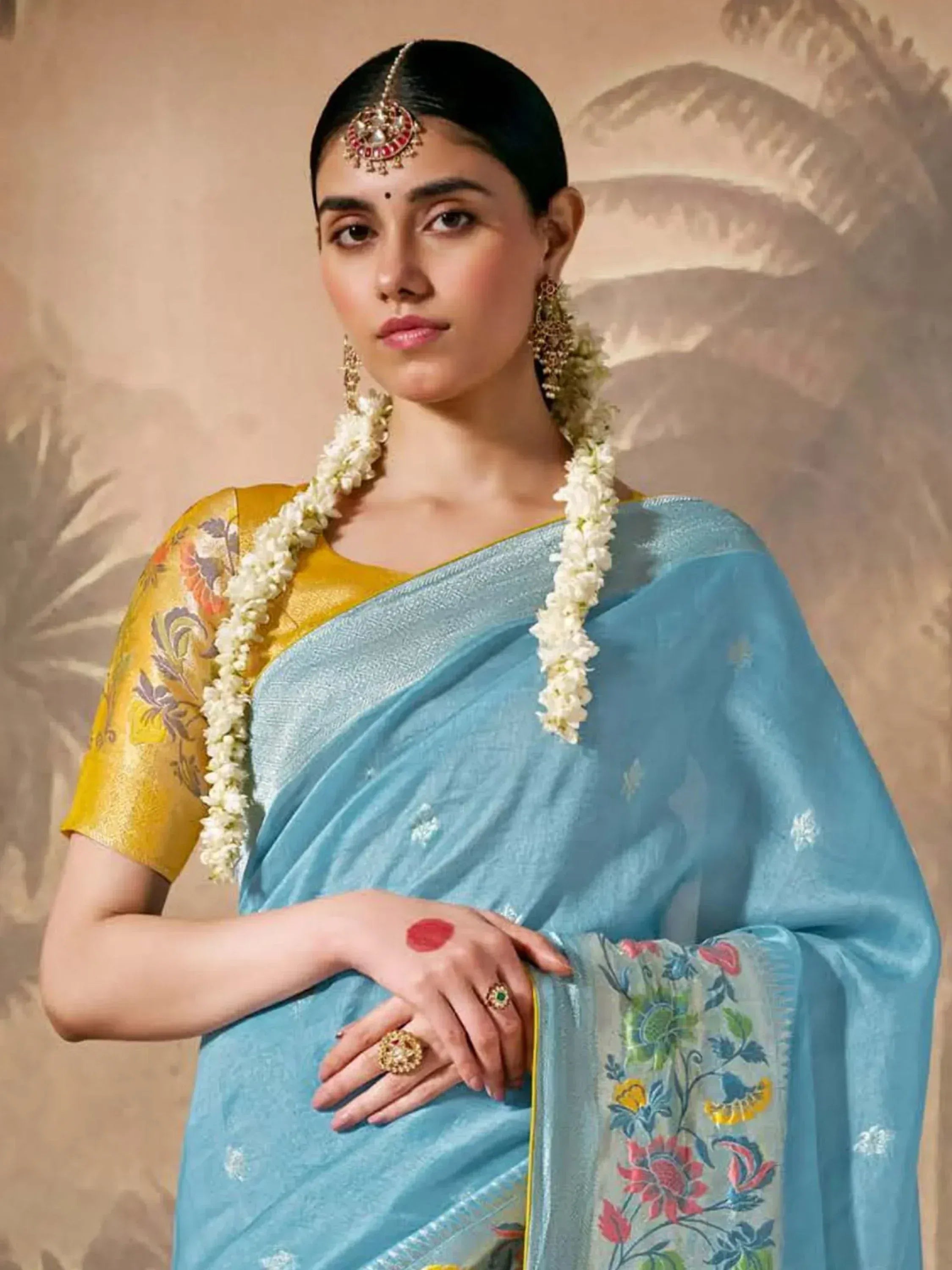 Woman in light blue floral saree with yellow blouse, traditional jewelry, and jasmine garland