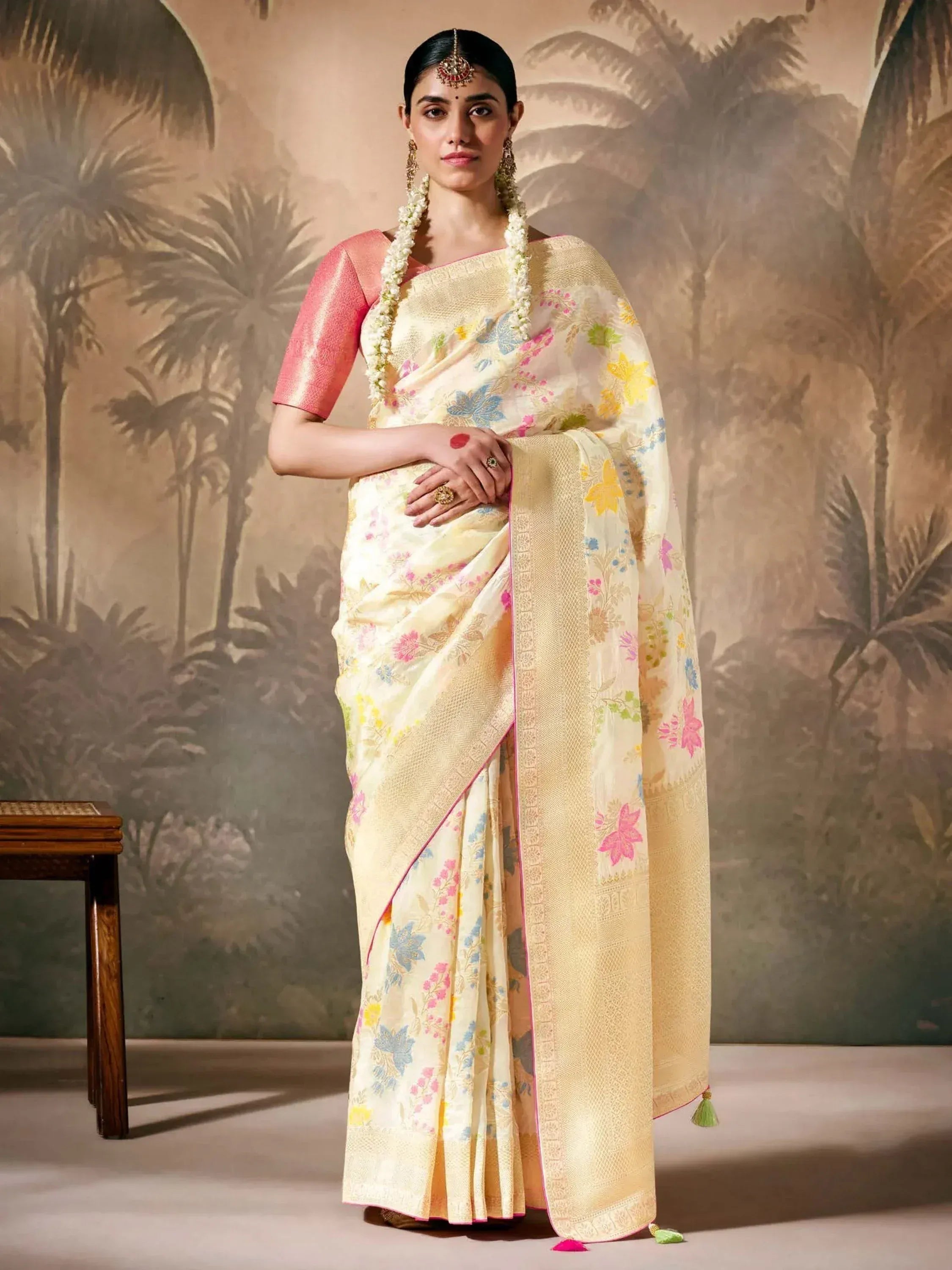 Cream floral saree with pink blouse, gold border, and tassels, styled with traditional jewelry for ethnic wear.